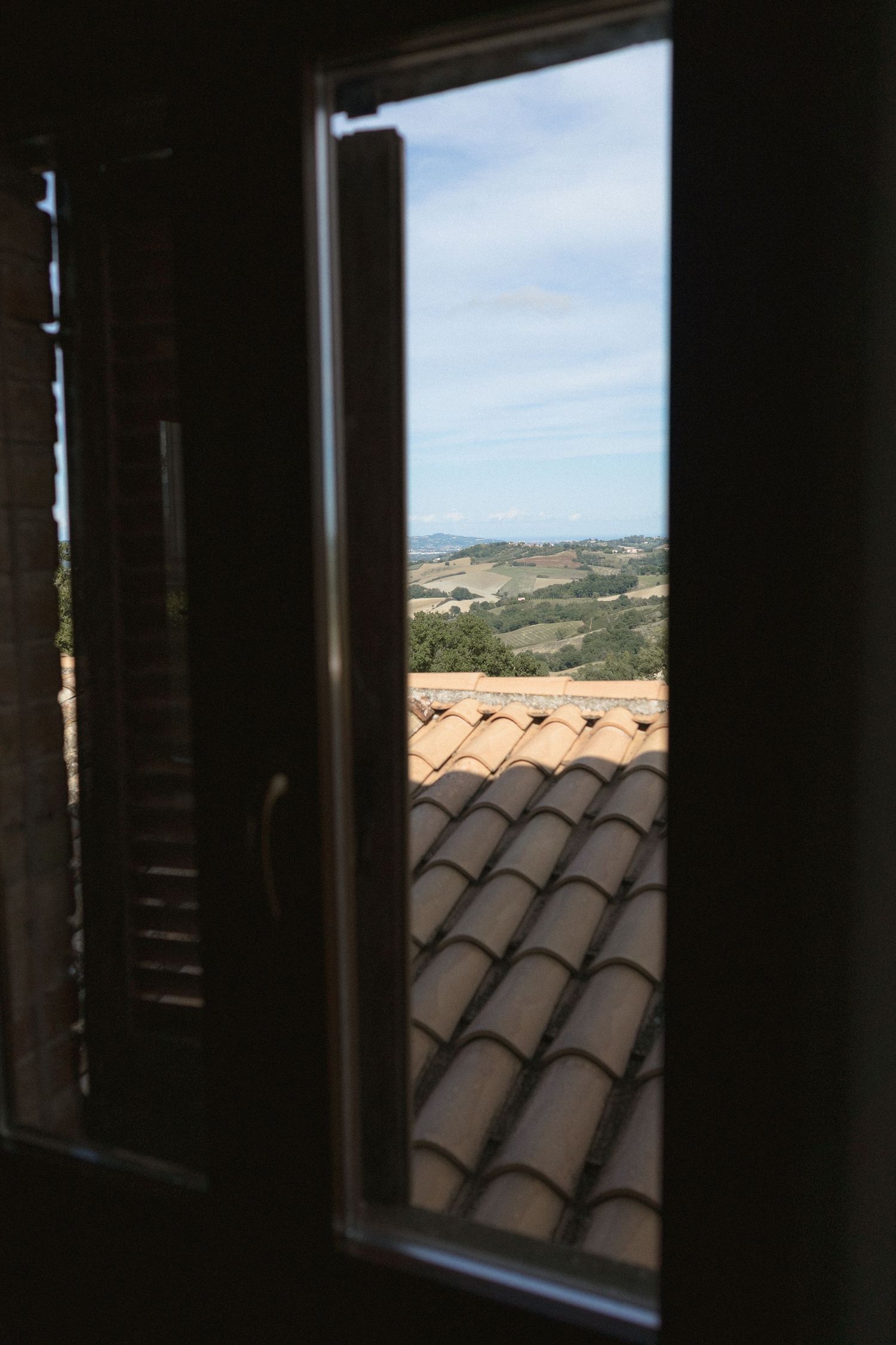 View through dark window frames showing terracotta roof tiles and rolling hills in the distance.