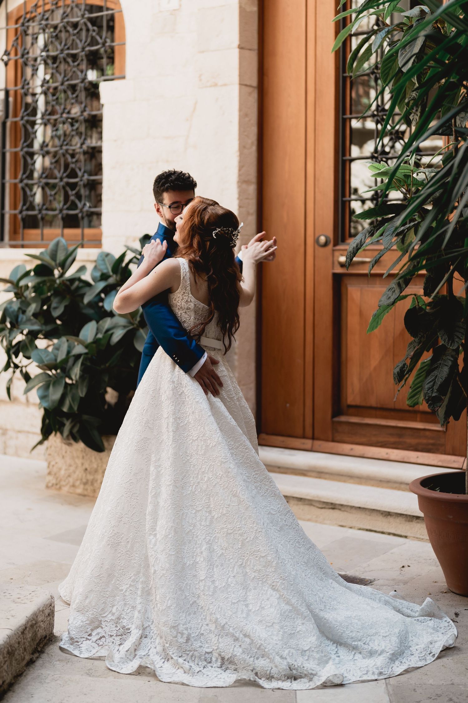 Wedding couple embracing on stone steps with trailing white dress and elegant architecture.