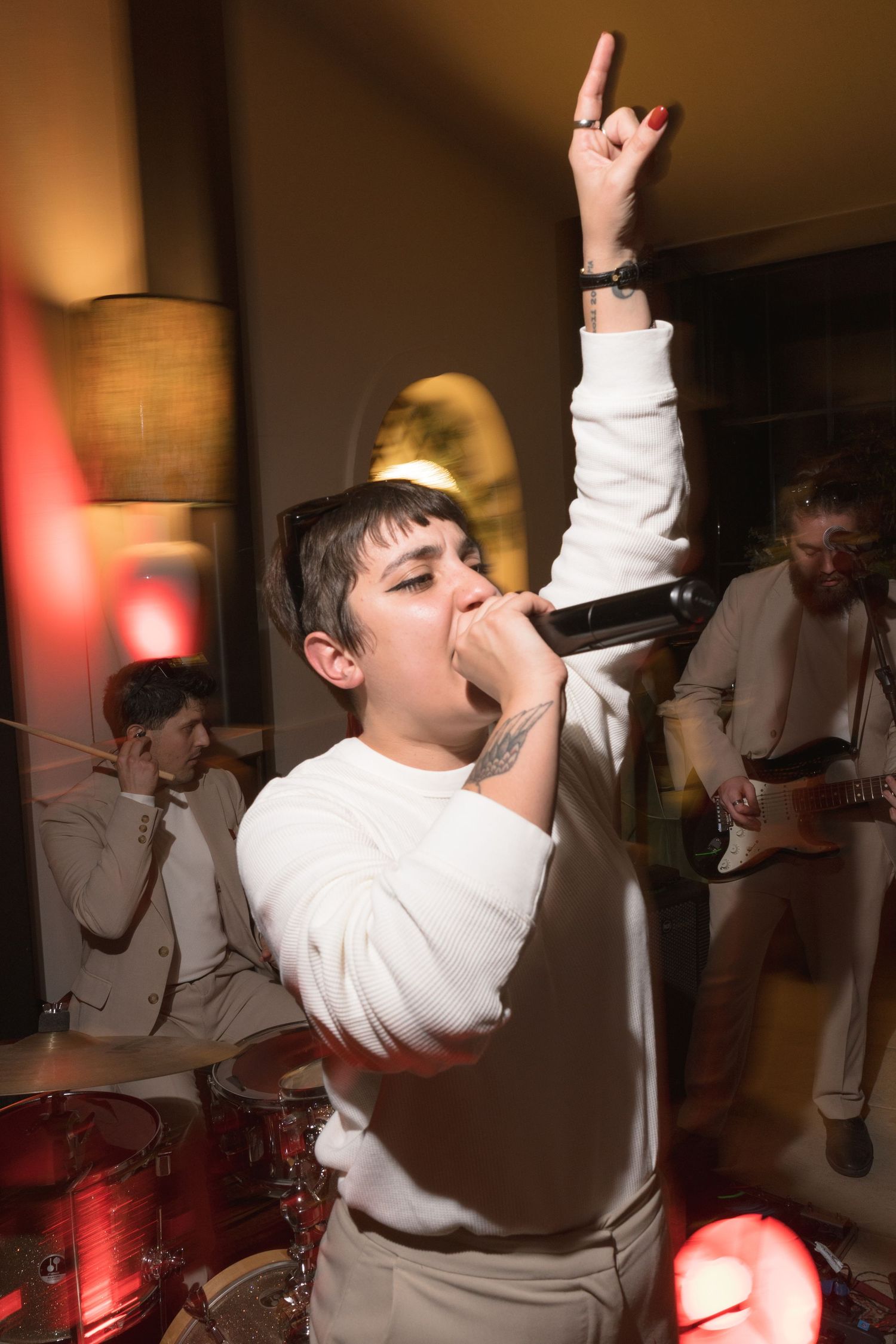Energetic singer in white outfit performs with microphone and band at wedding reception.