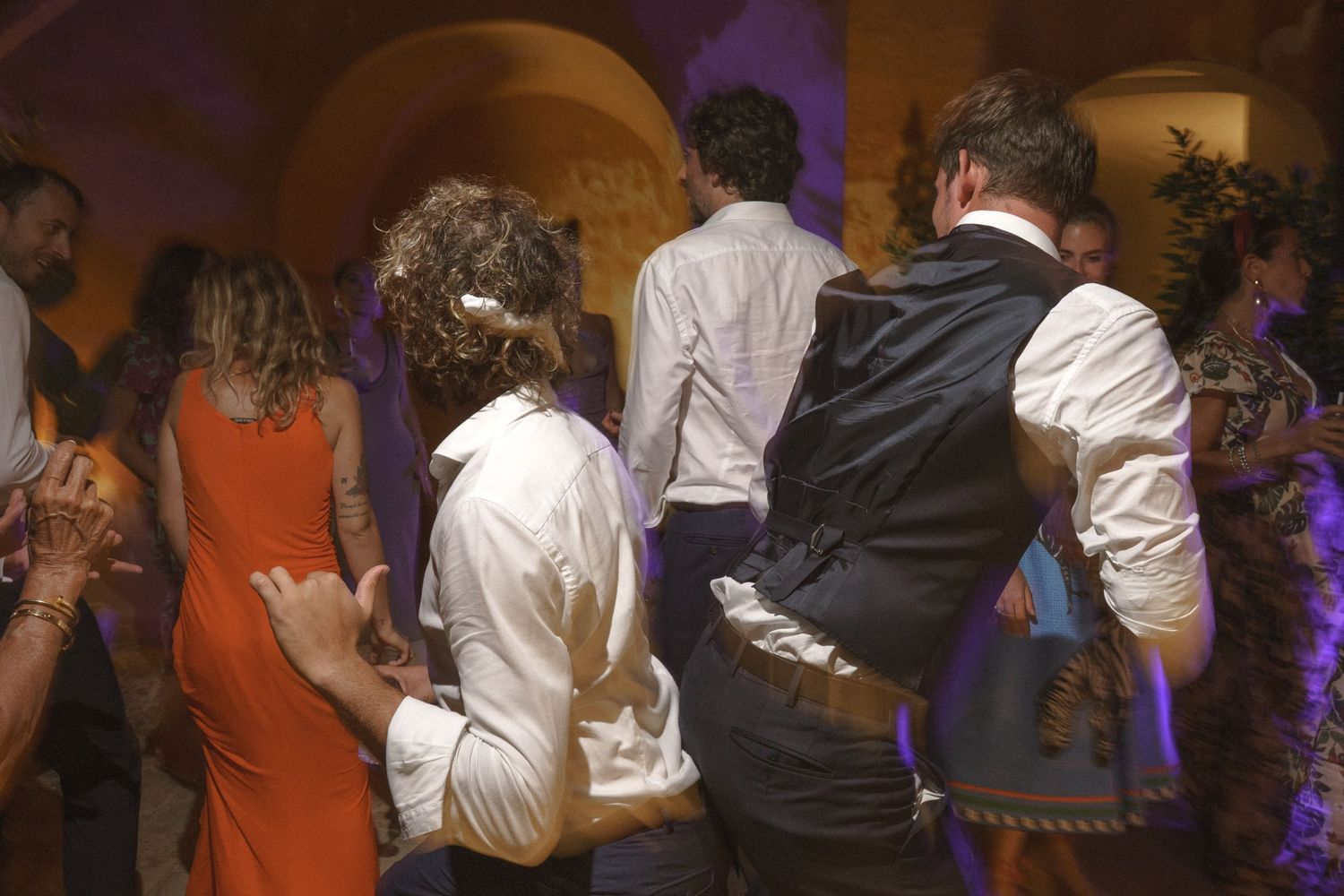 People dancing at a wedding reception with colorful purple lighting and stone arches.