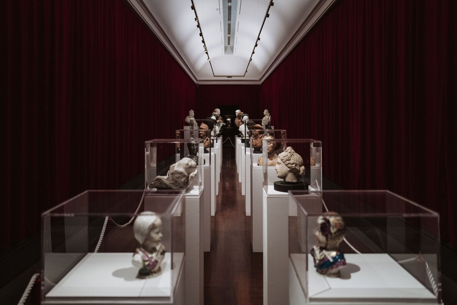 Museum exhibition hall with symmetrically displayed artifacts in glass cases along a red-walled corridor.