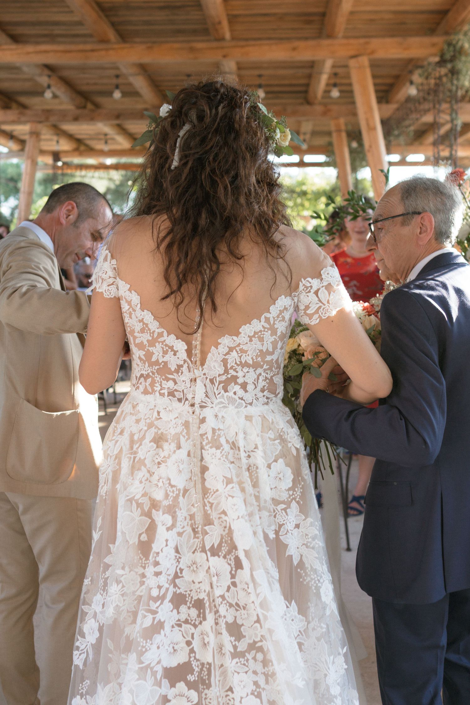 Back view of an intricate lace wedding dress with sheer details during an outdoor celebration.