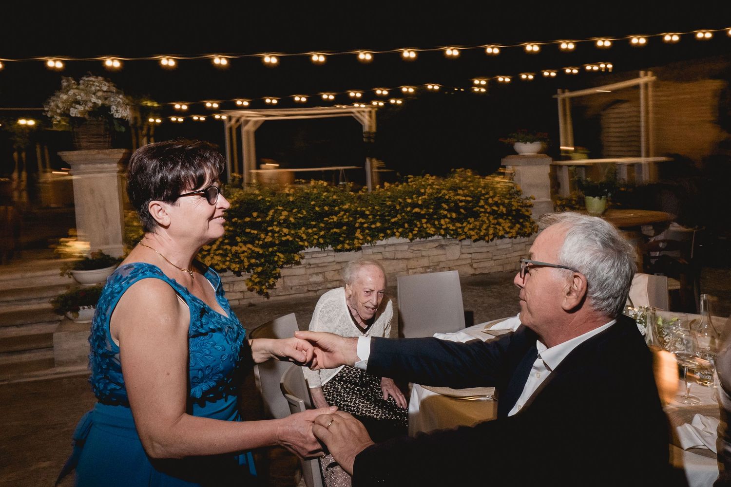 People dancing and enjoying an evening outdoor celebration under decorative string lights at a casual party.