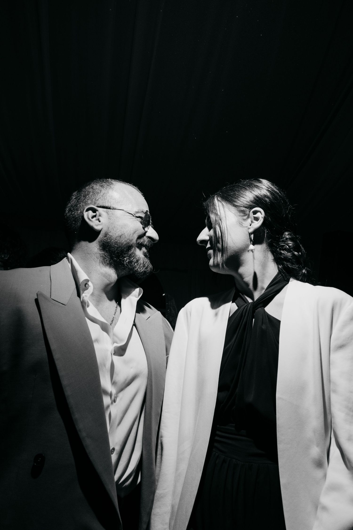 Artistic black and white portrait of two people in white attire against dark background.