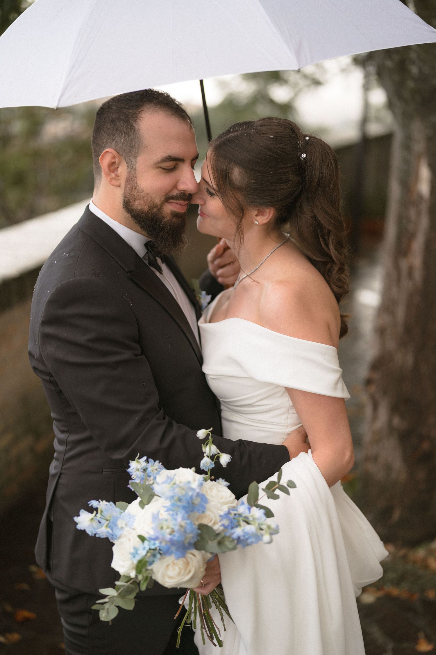 A romantic wedding portrait shows a couple embracing while holding a bouquet with blue and white flowers.