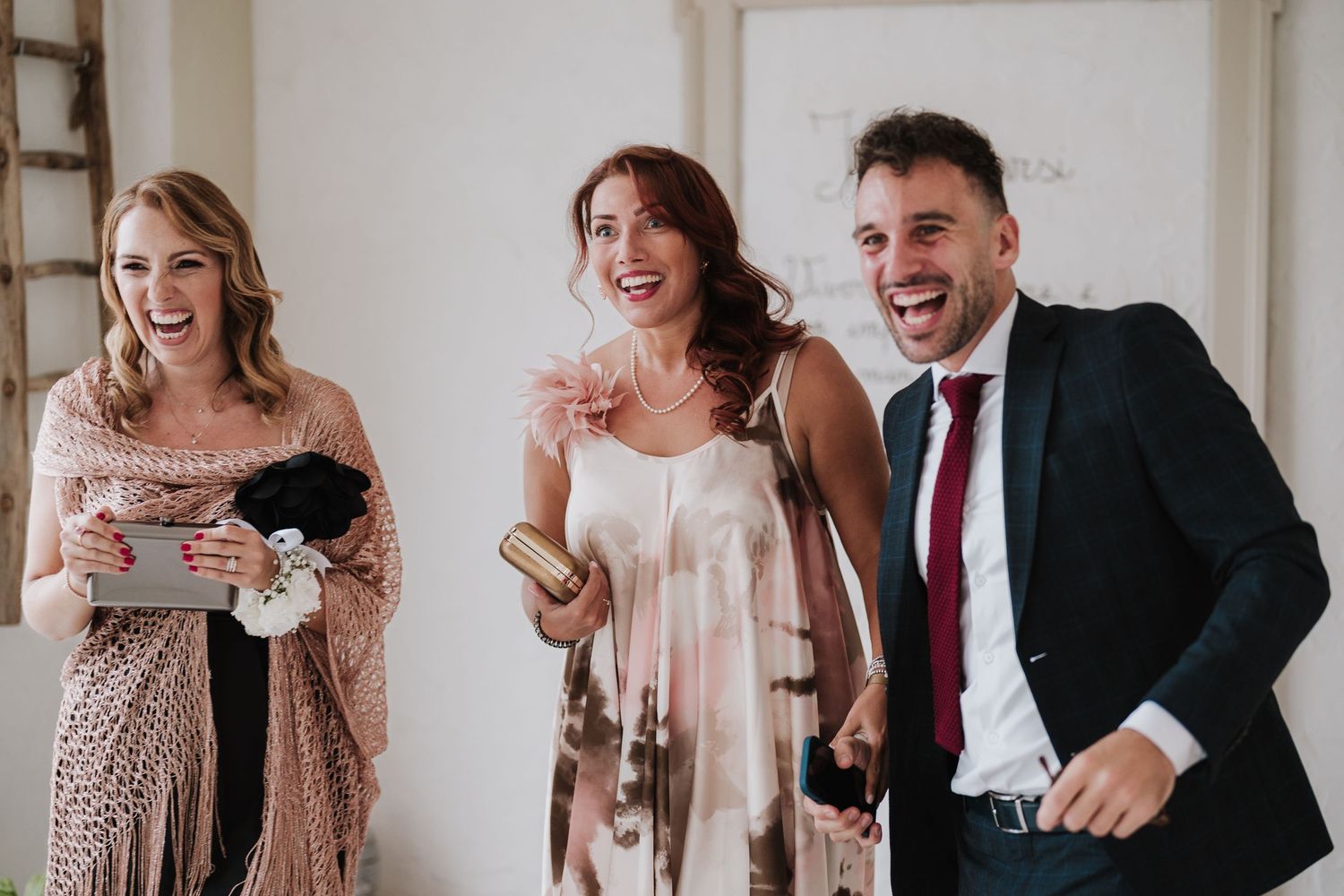 Candid moment of three wedding guests laughing and celebrating in formal attire.