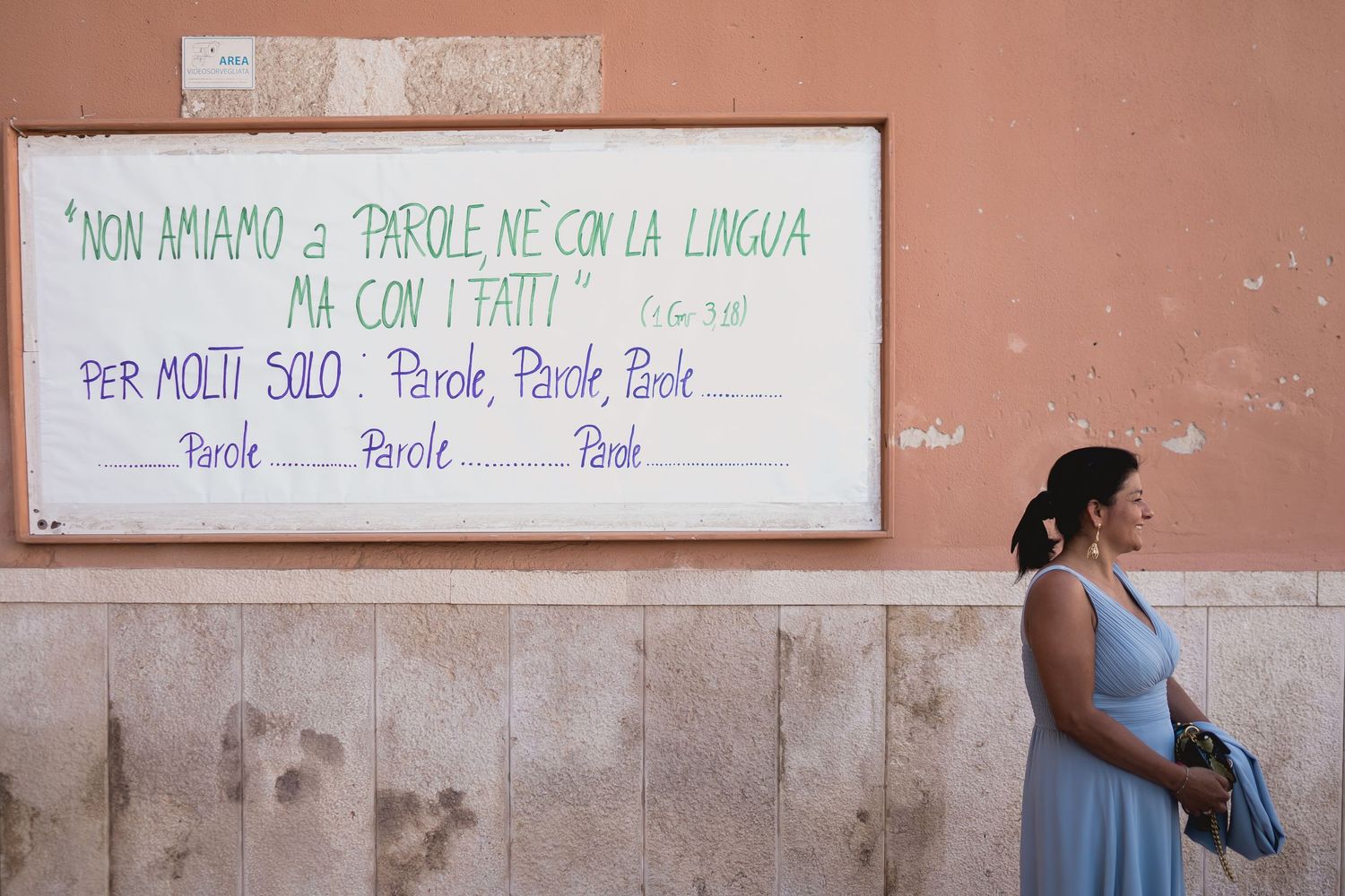 A street scene with text written on a pink wall and someone standing nearby in a blue dress.
