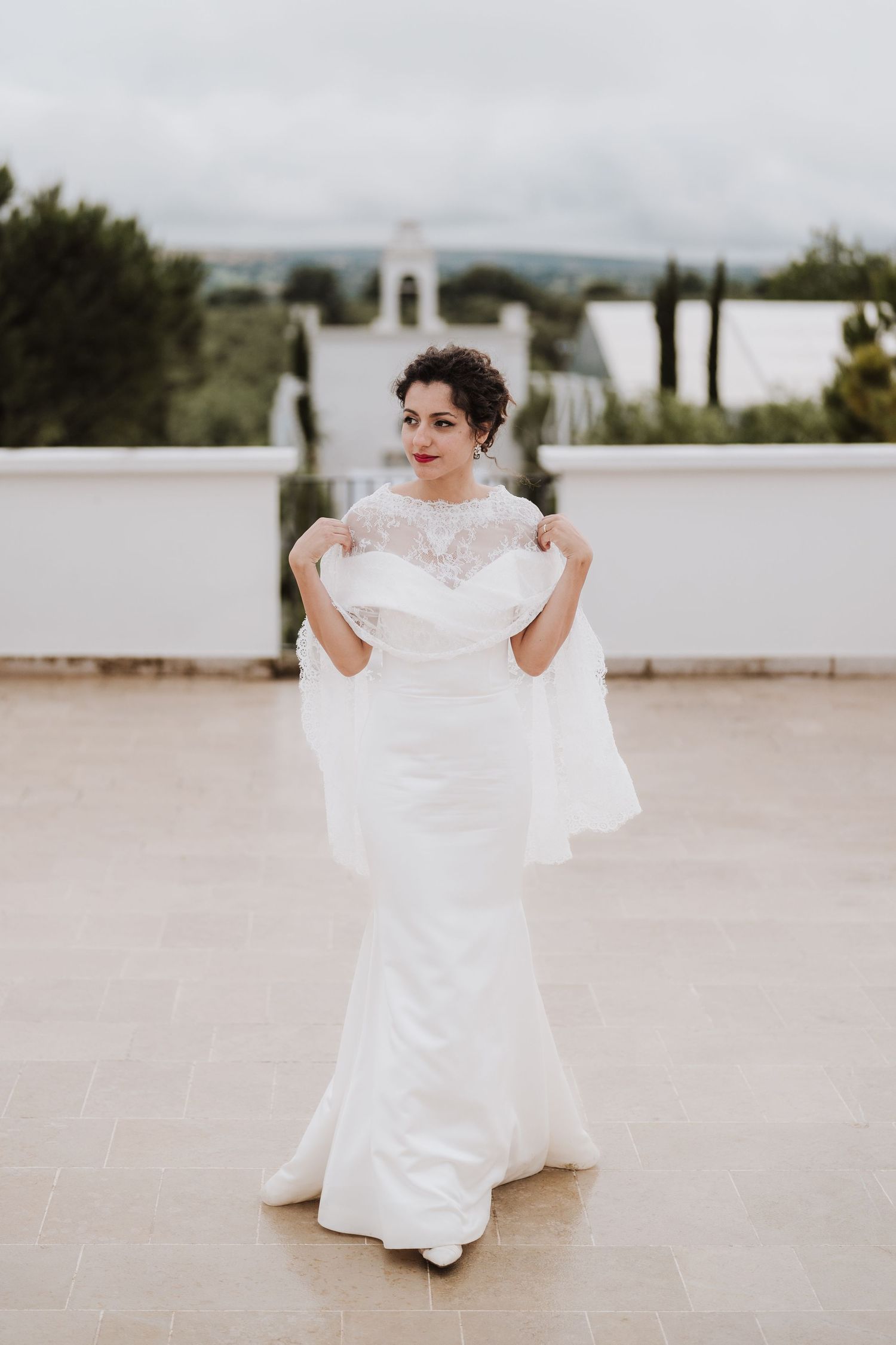 Elegant bridal portrait showcasing a fitted white wedding gown with lace details on a terrace.