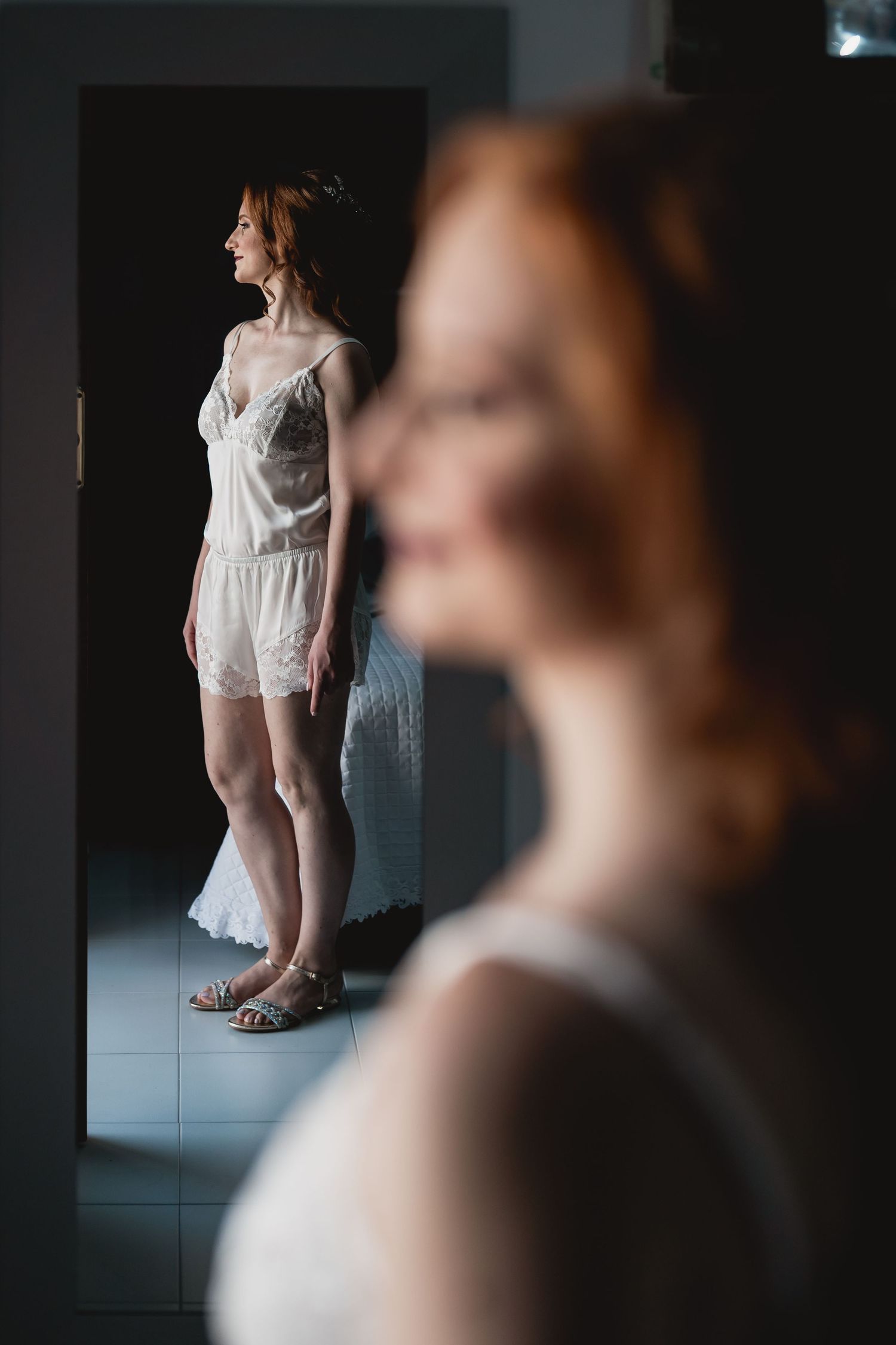 Artistic mirror reflection showing white lace bridal attire in moody lighting.