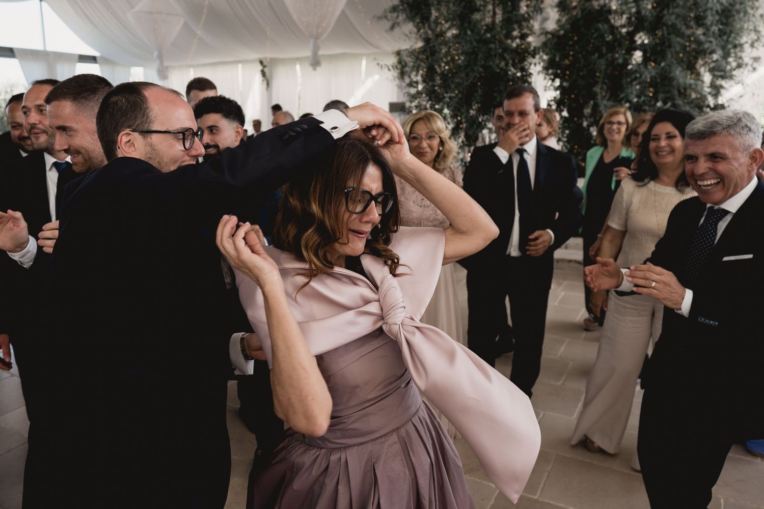 Guests dancing and celebrating at a wedding reception under a white draped tent ceiling.