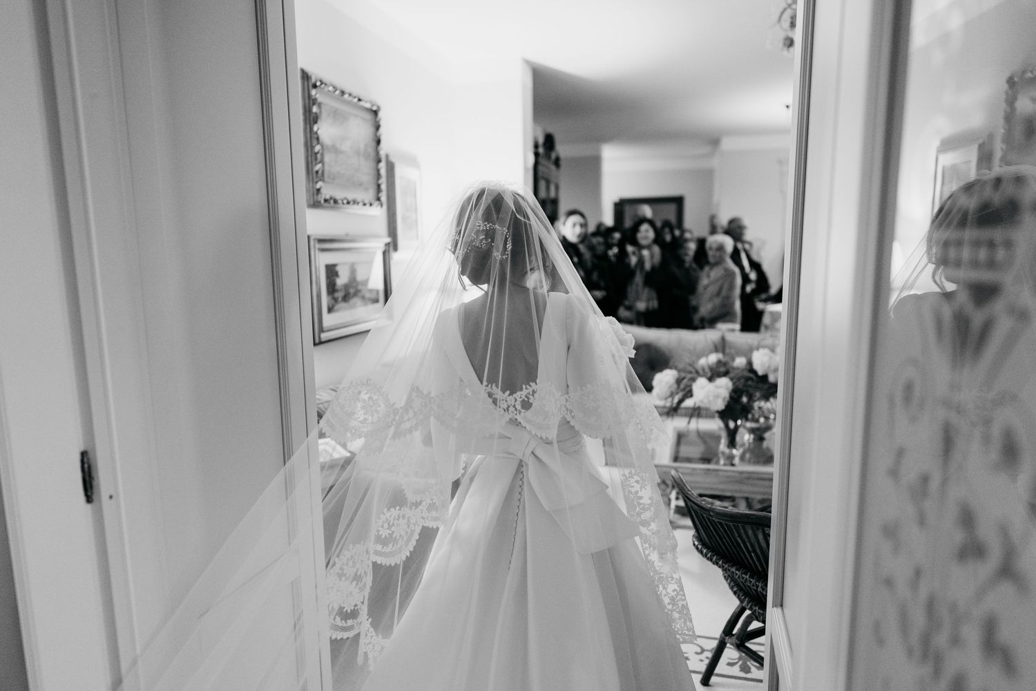 Black and white photo of bride in lace wedding dress and veil walking through doorway before ceremony.