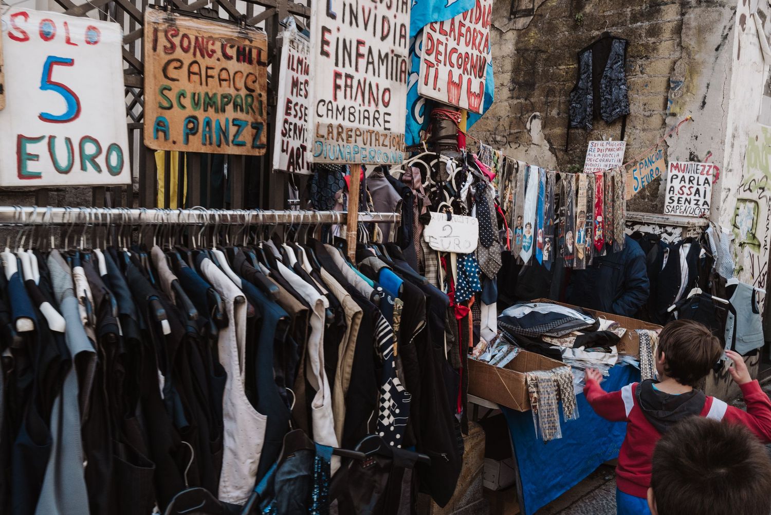 Second-hand clothing market stall with racks of clothes and price signs in euros.