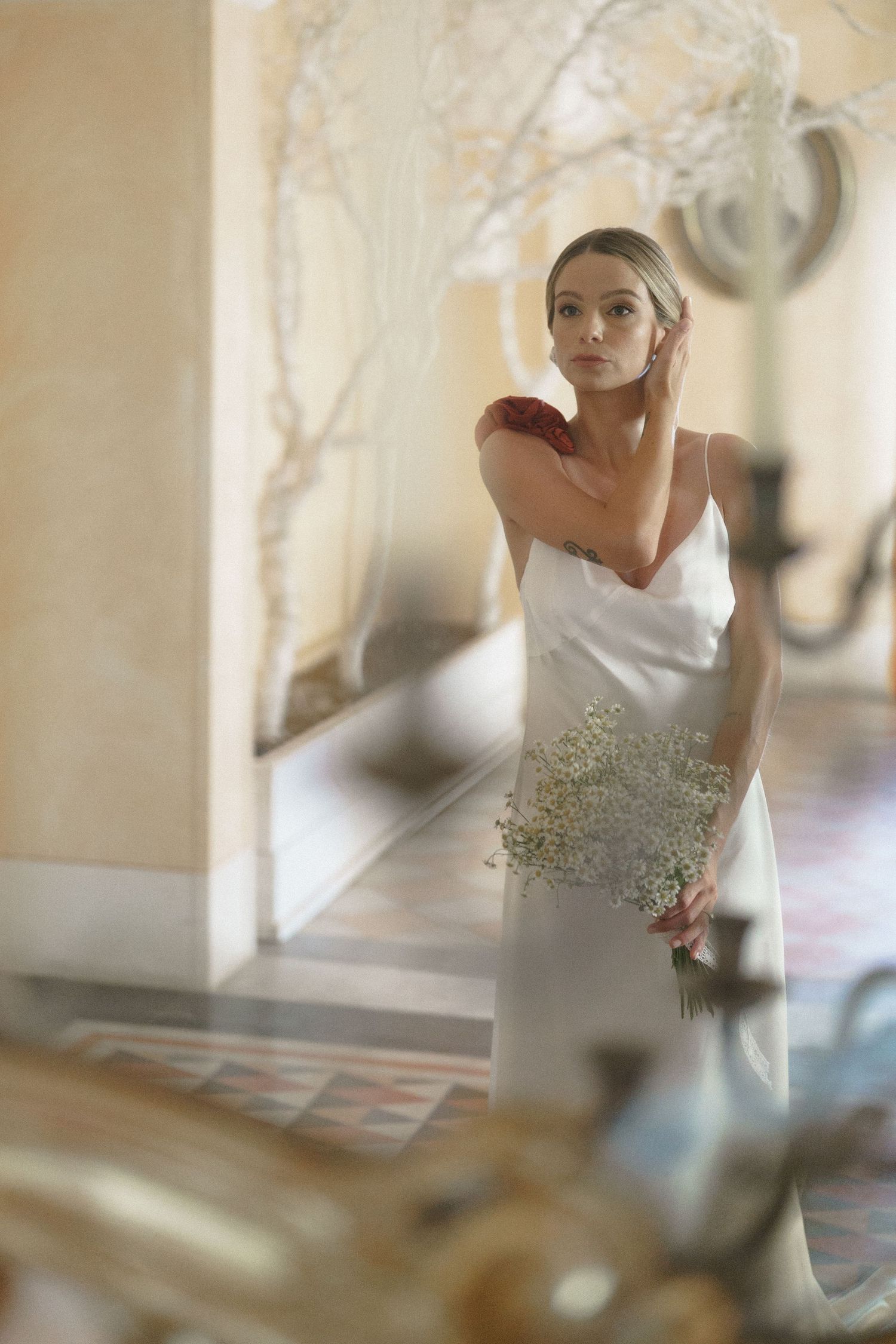 A bride in a strapless white dress with beaded detail poses elegantly in a sunlit room with soft ethereal lighting.