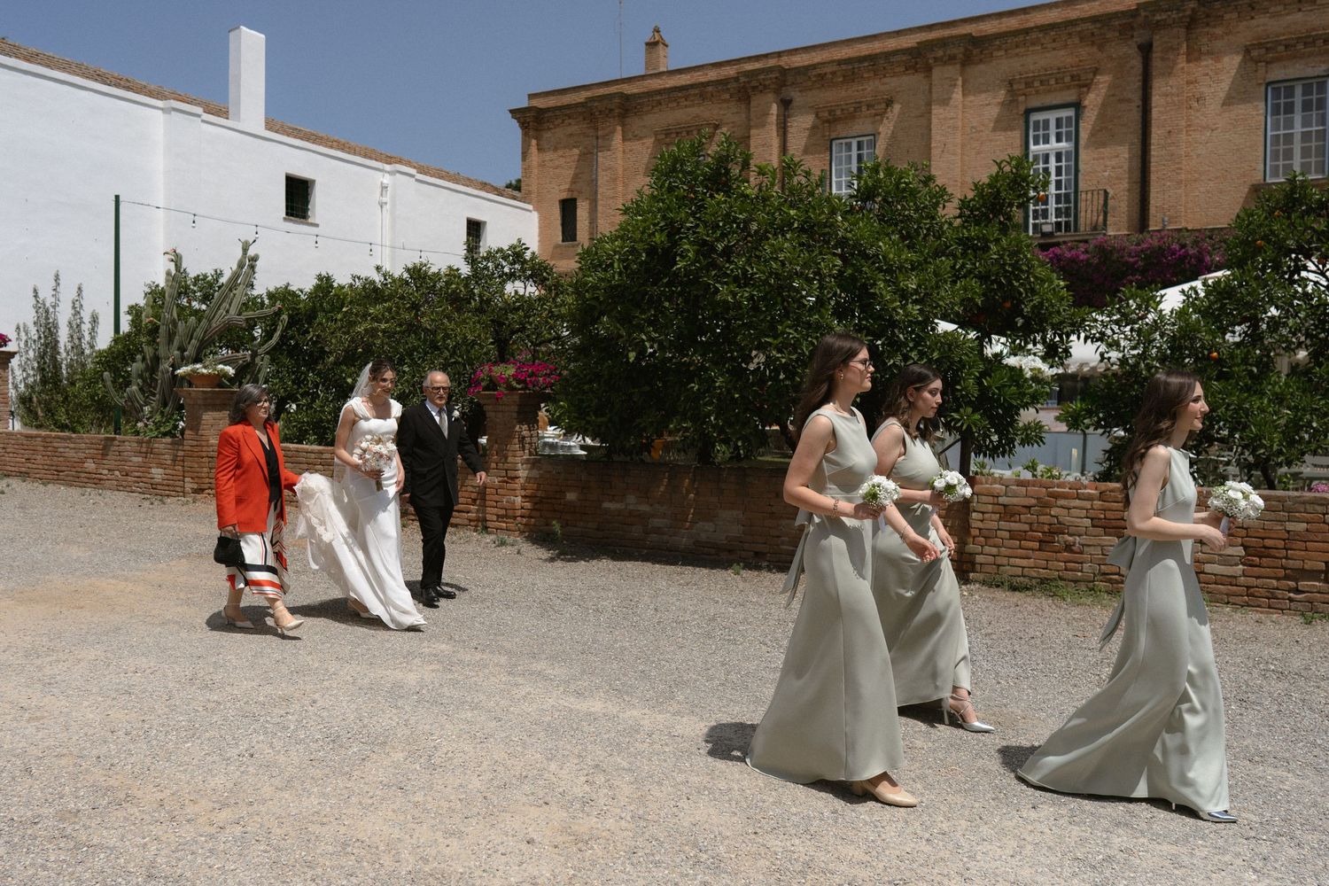 Wedding guests gather in an elegant stone courtyard with arched architecture and natural lighting.