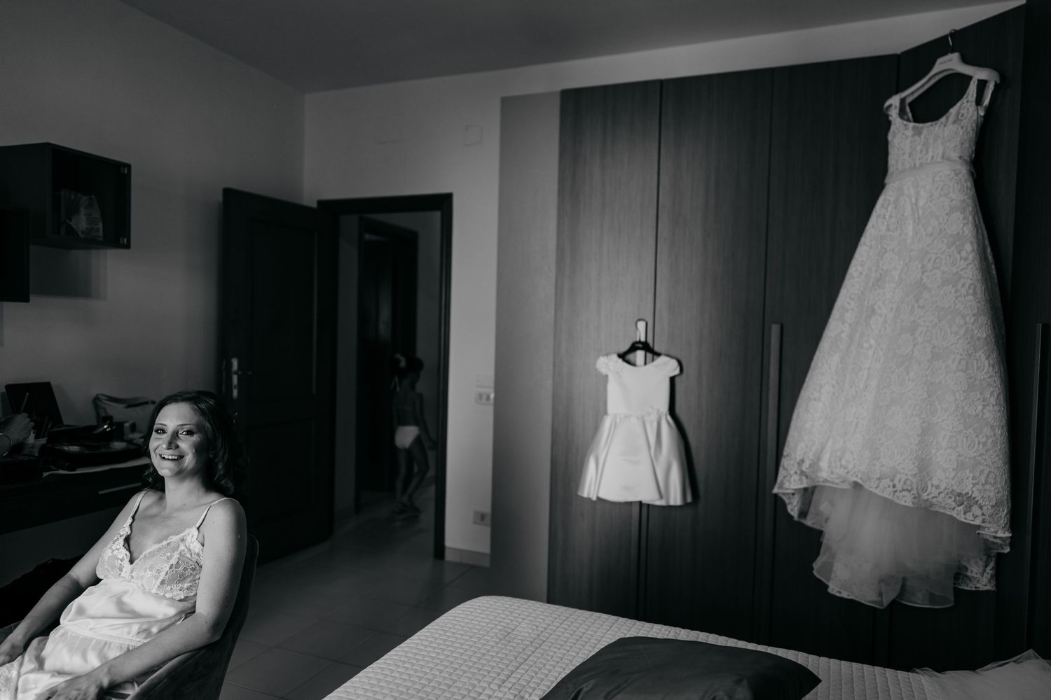 Black and white photo of wedding dresses hanging in a room's preparation space.