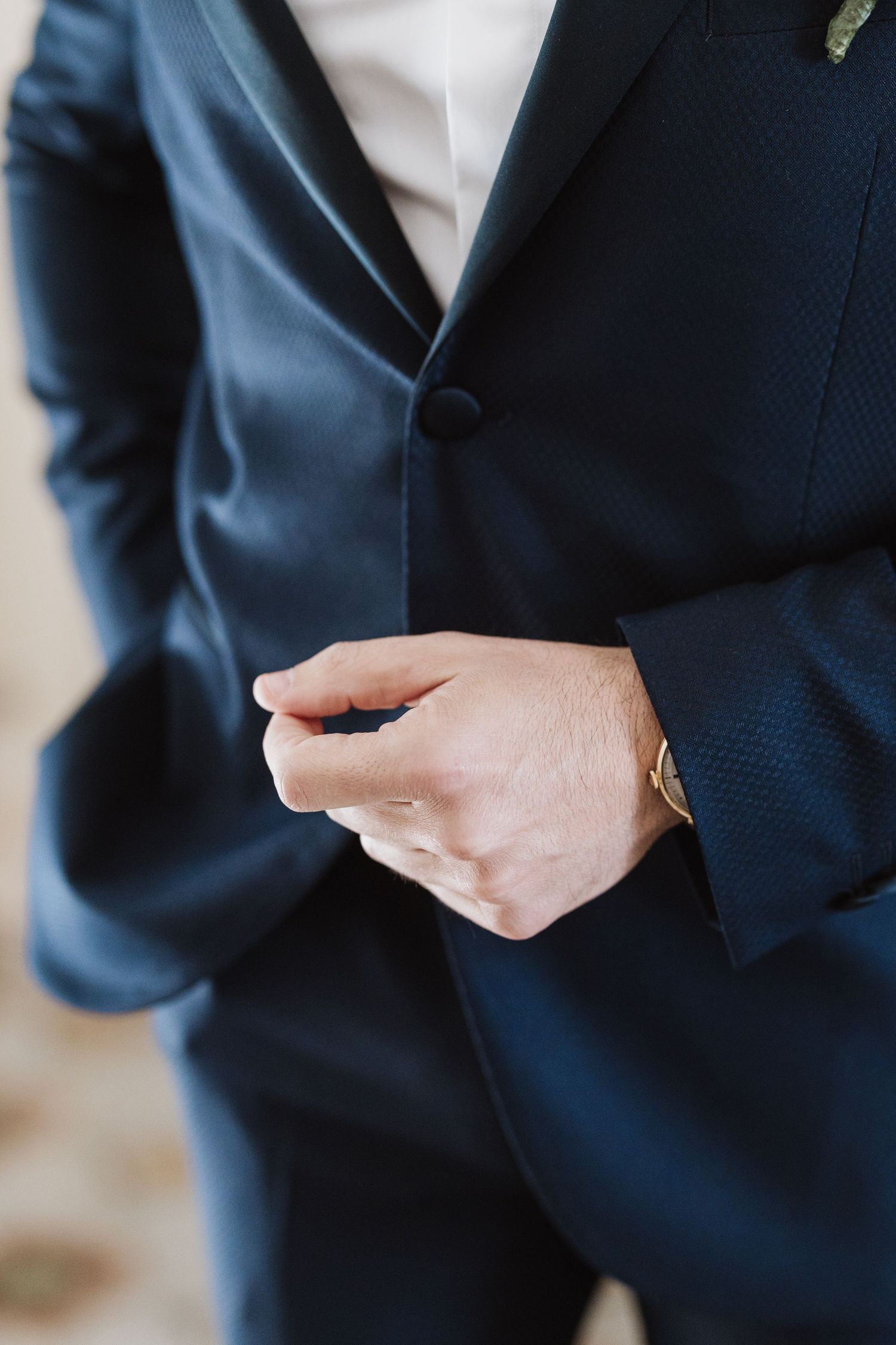 Close-up of hands adjusting buttons on a navy blue formal suit jacket.