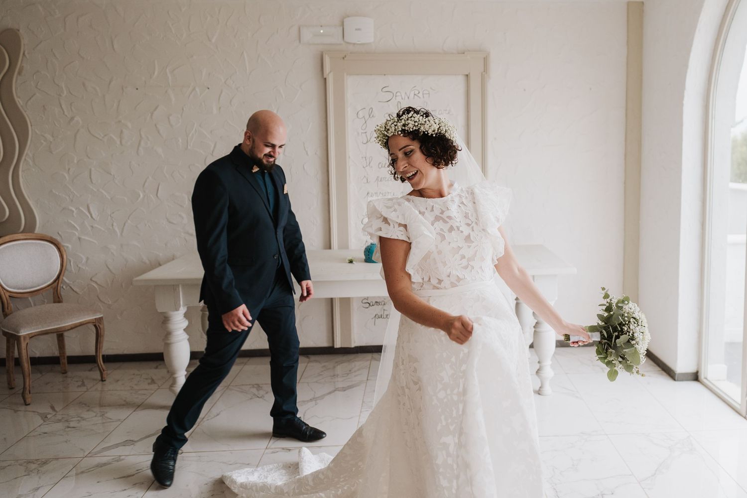 Wedding moment captured in a white interior room with arched windows and elegant decor.