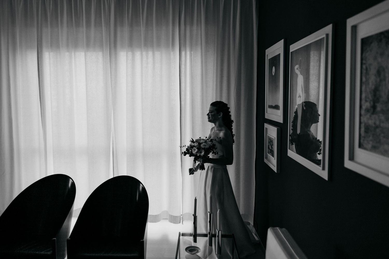 A silhouette stands by a window holding flowers in a minimalist black and white composition.