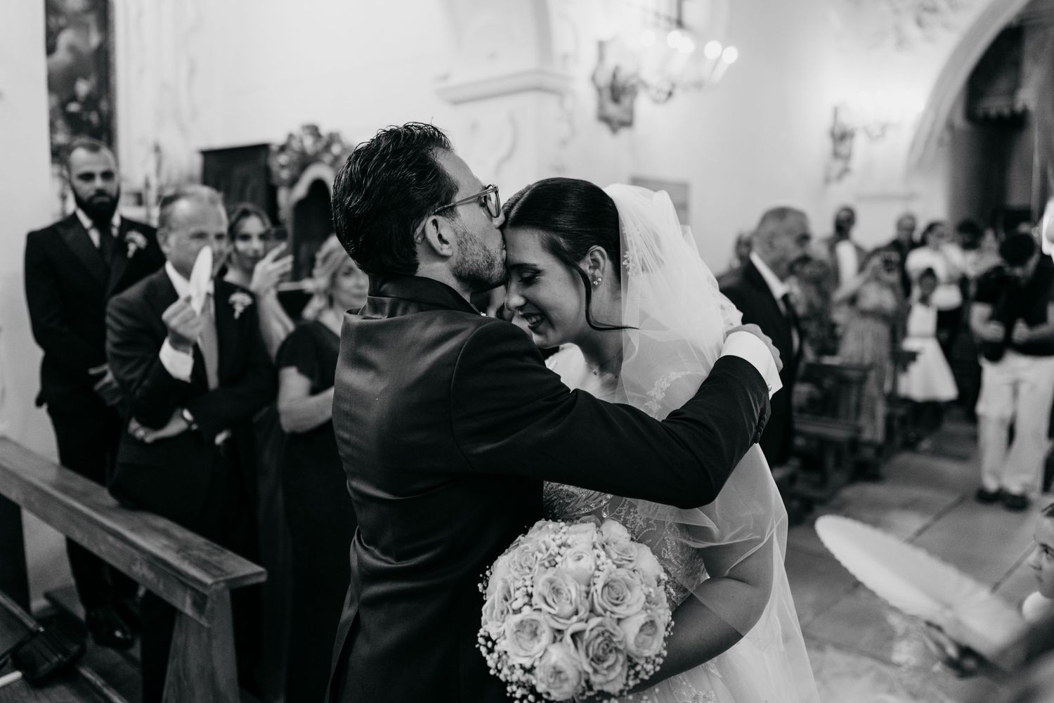 An emotional black and white photograph of an embrace during a church wedding ceremony.