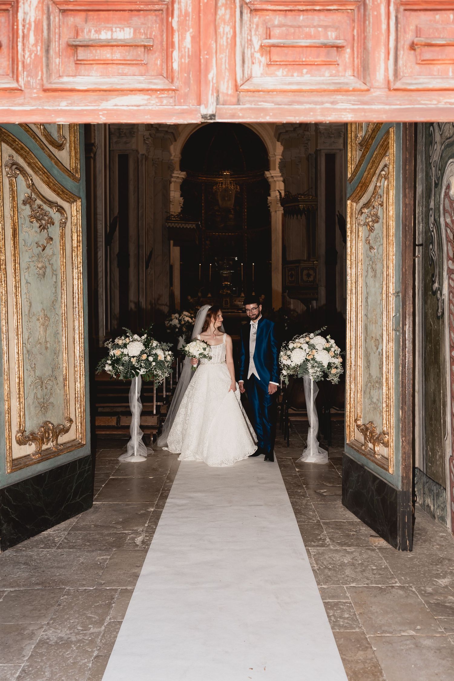 Wedding ceremony setup in an elegant church interior with white floral arrangements and ornate decor.