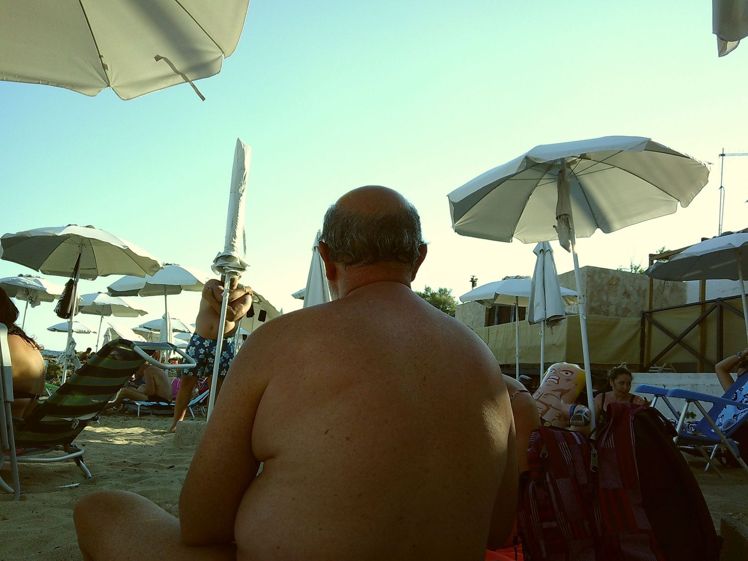 Back view of beachgoer sitting under white umbrellas by the ocean.