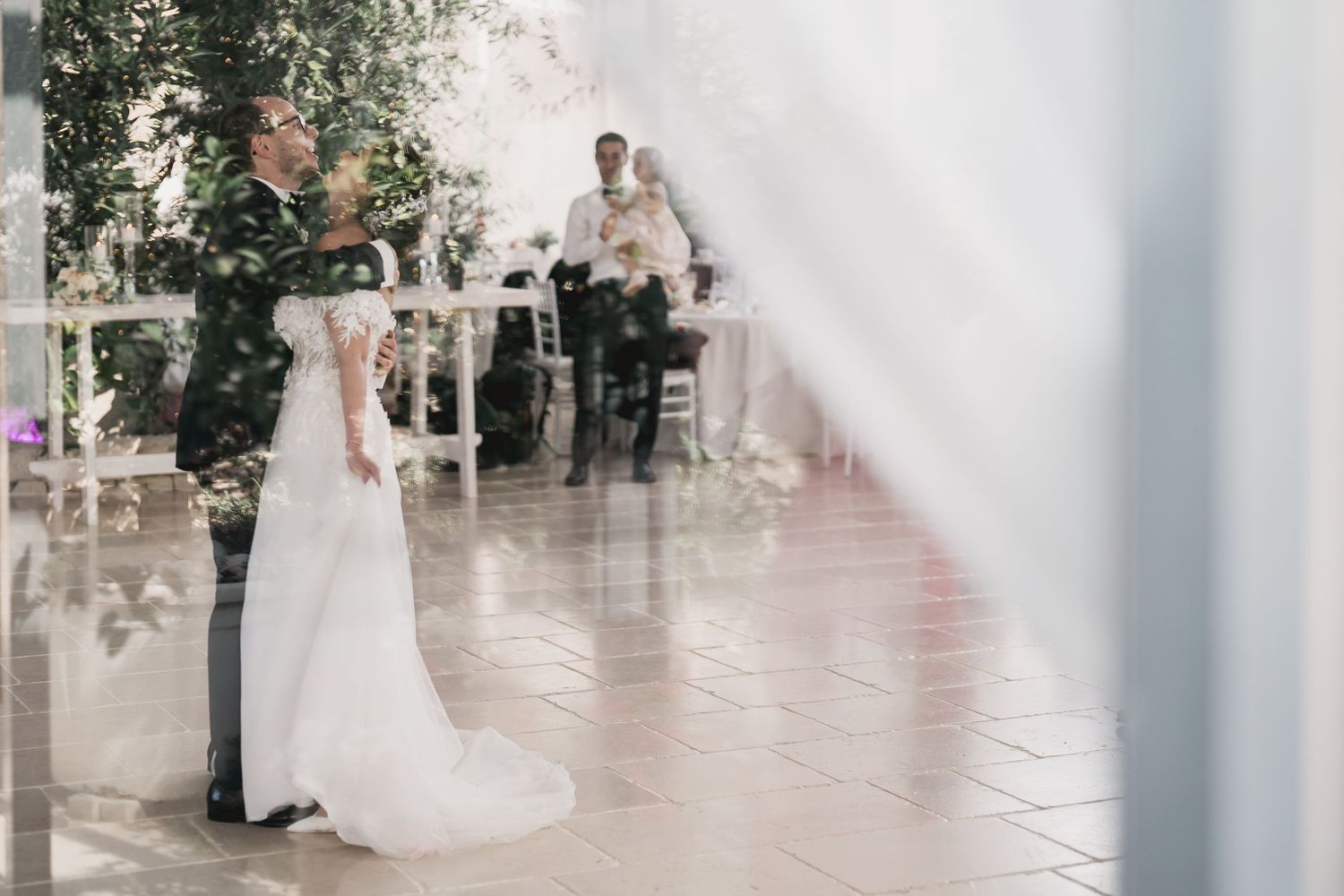 Romantic wedding moment captured through sheer white curtains in an elegant venue.