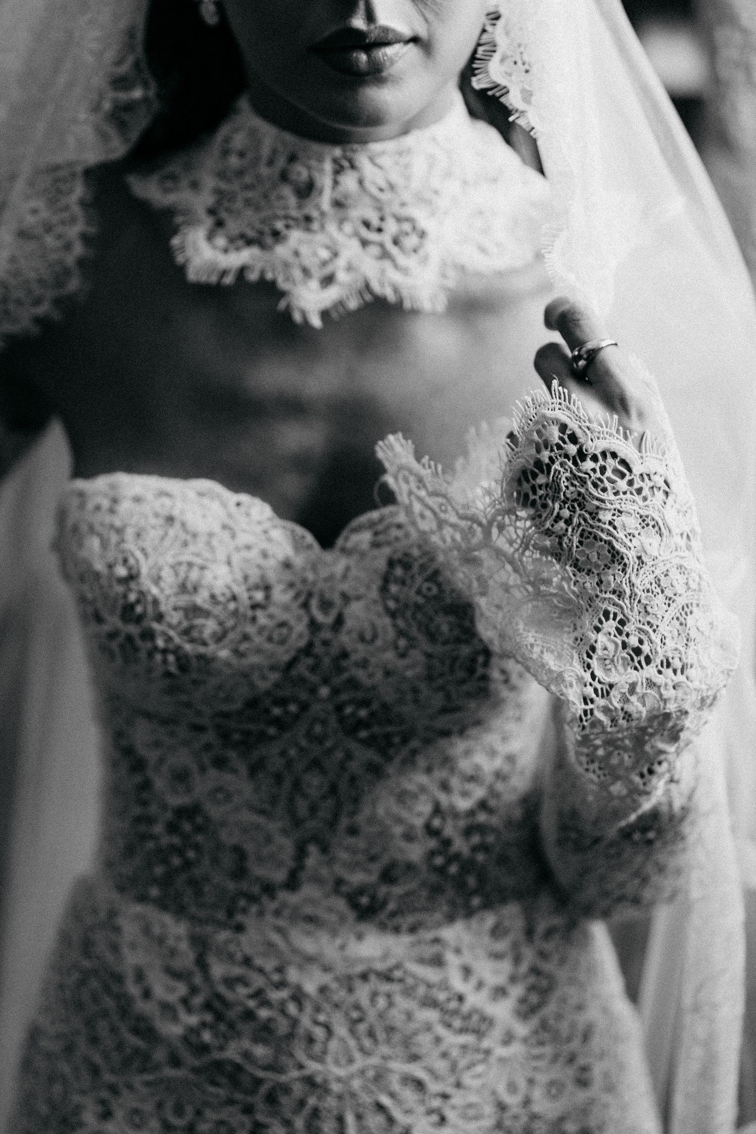 Black and white close-up of a bride's lace bodice, high lace collar, and long lace glove sleeve with a ring.
