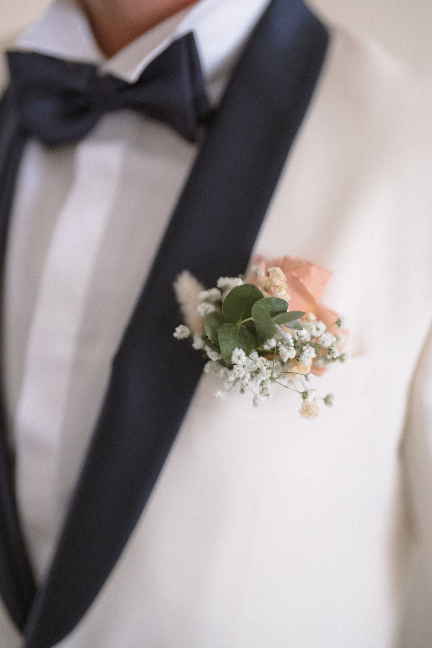 A close-up detail of a white boutonniere with delicate baby's breath flowers pinned to a black tuxedo lapel.