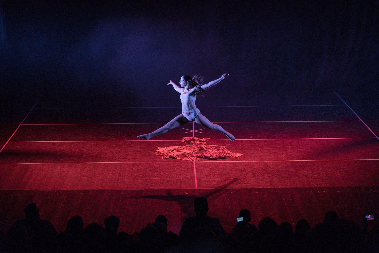Performer leaps across red-lit stage during dramatic solo performance.