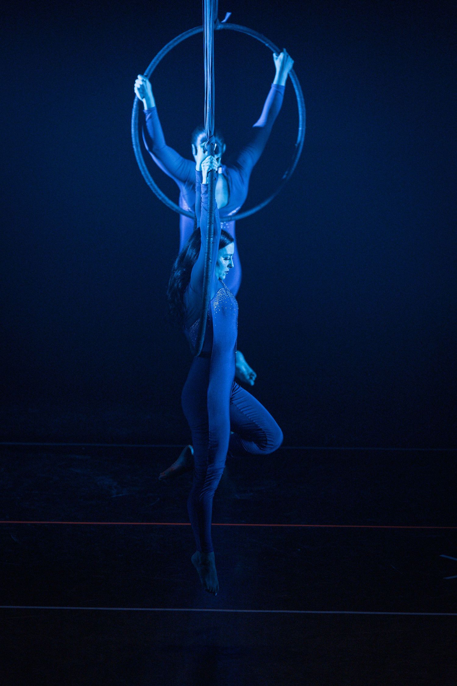 Aerial artist performs on illuminated hoop in ethereal blue lighting.