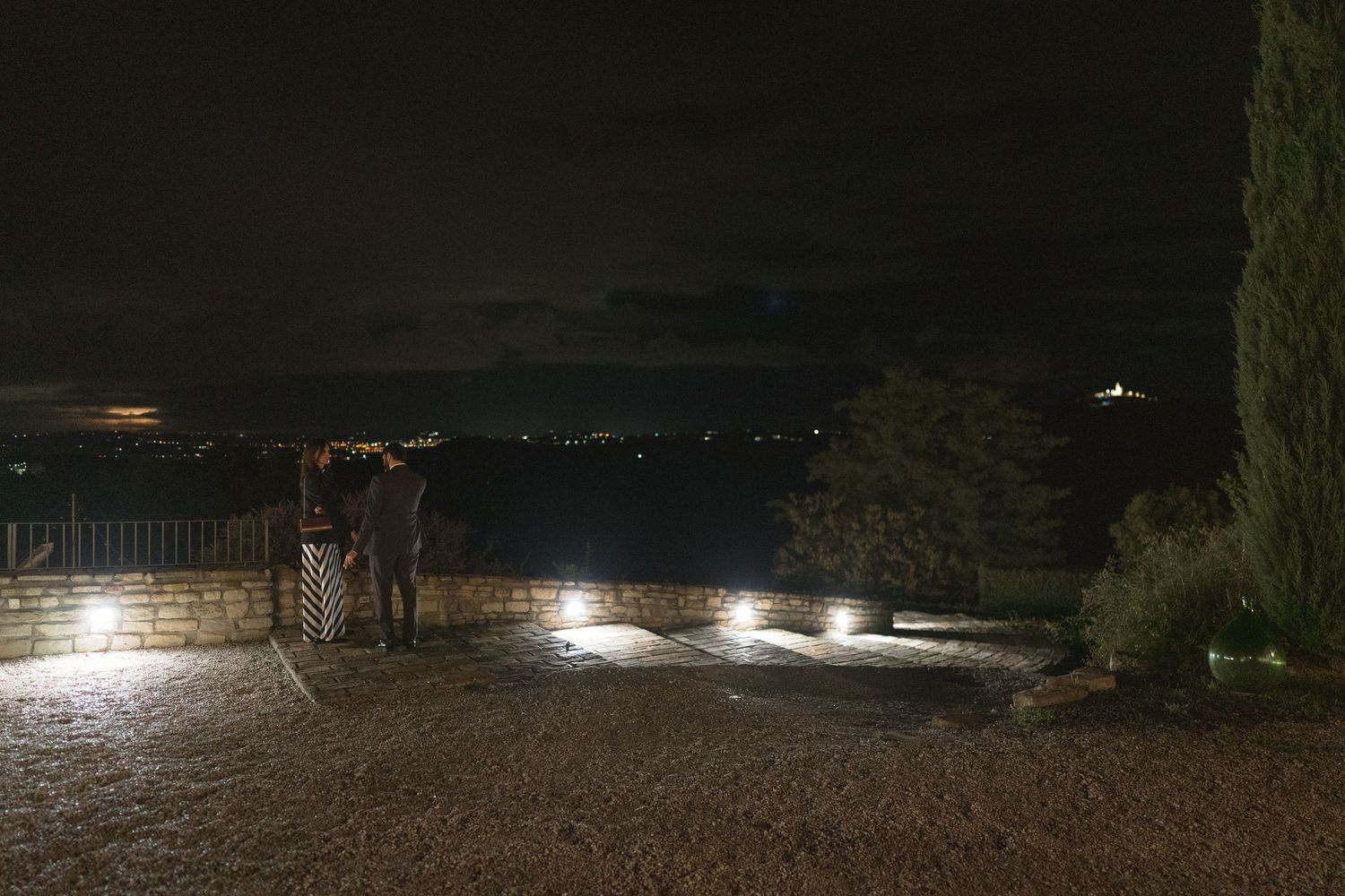 Silhouette of a couple overlooking city lights at night from a terrace.