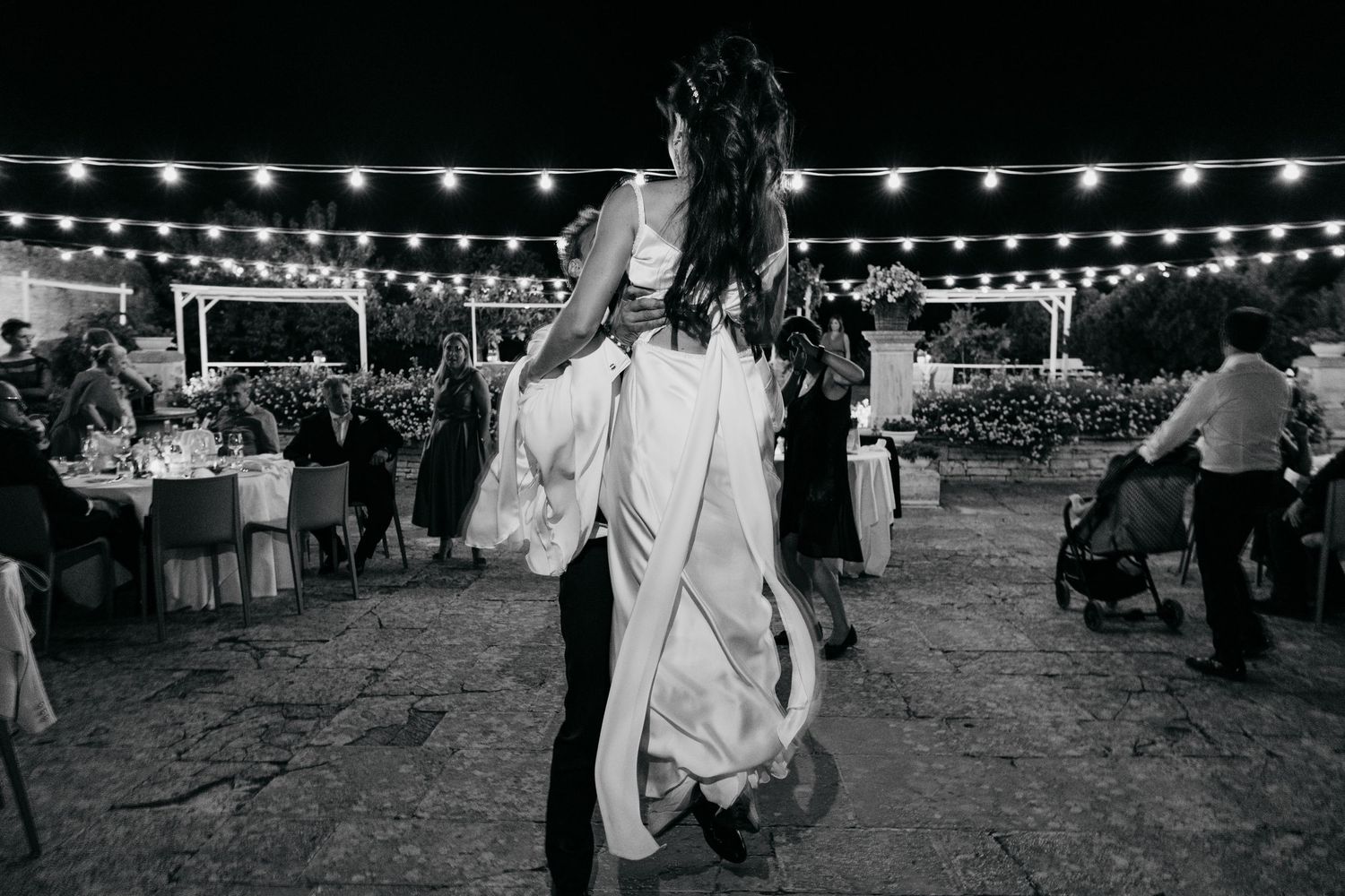 A couple dances beneath twinkling lights at an outdoor wedding reception venue.