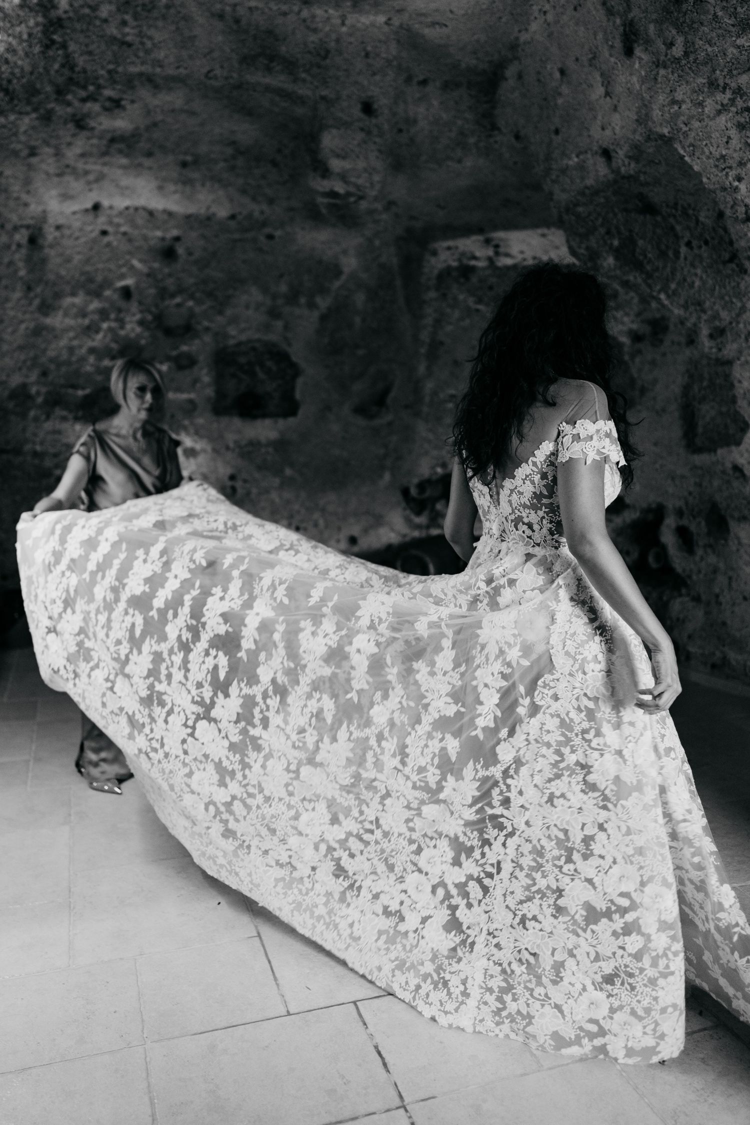 Person in a white lace dress reclining on a textured stone surface.