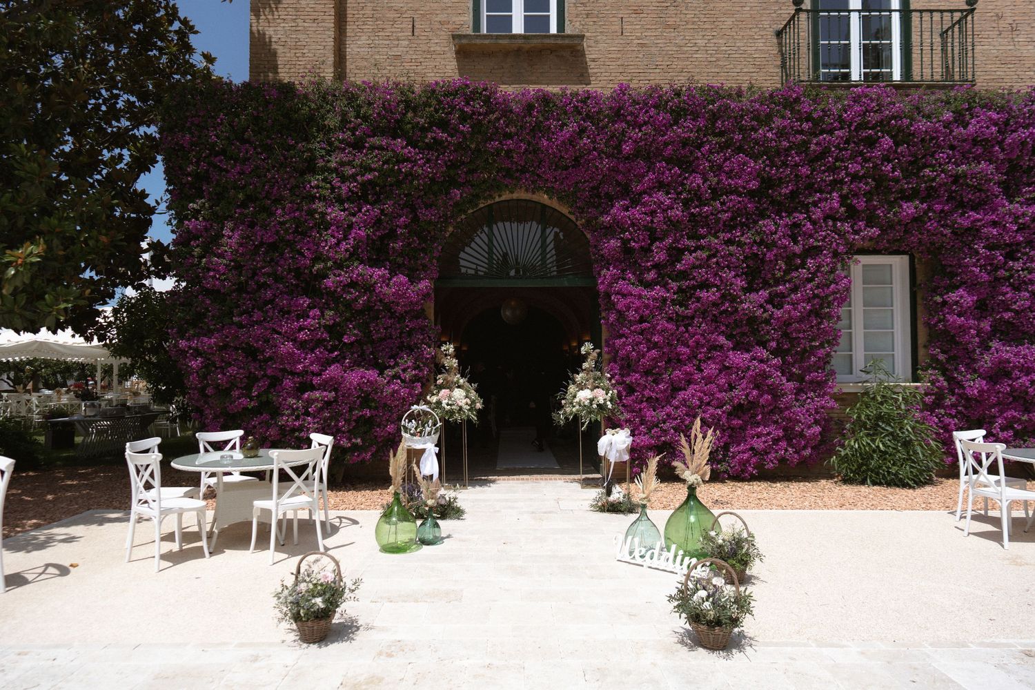 Stone patio with white chairs and vibrant purple bougainvillea flowers.