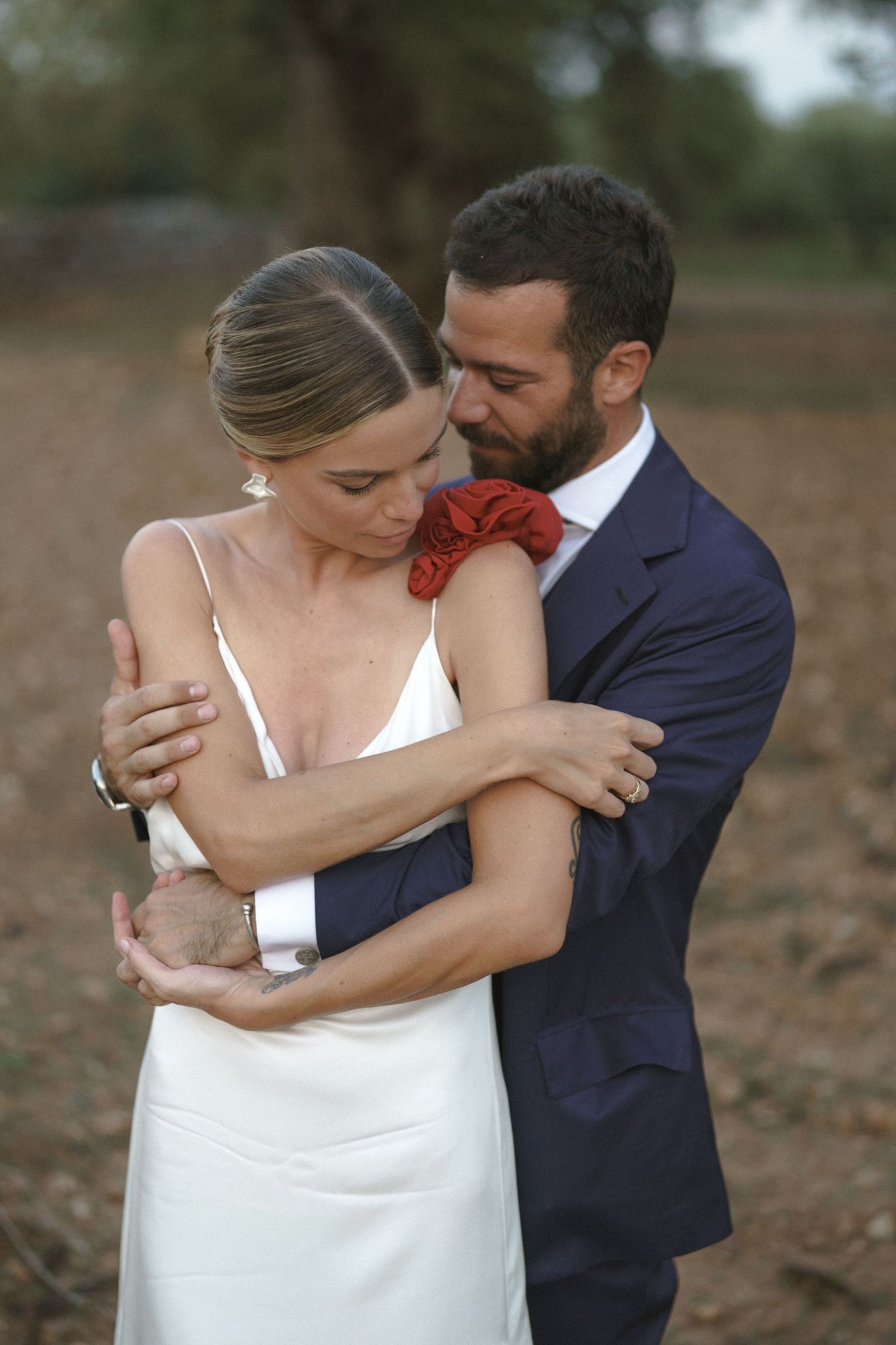 Intimate moment between couple in formal attire embracing against natural backdrop.