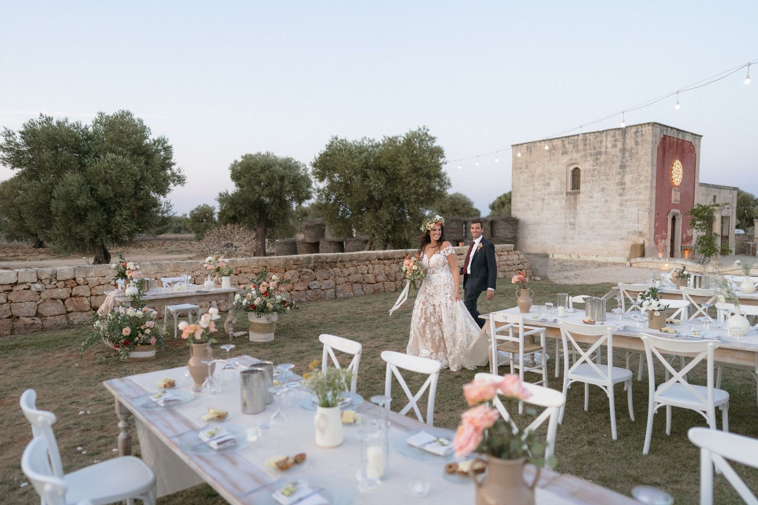 Elegant outdoor wedding reception setup with white chairs and tables in a rustic setting.