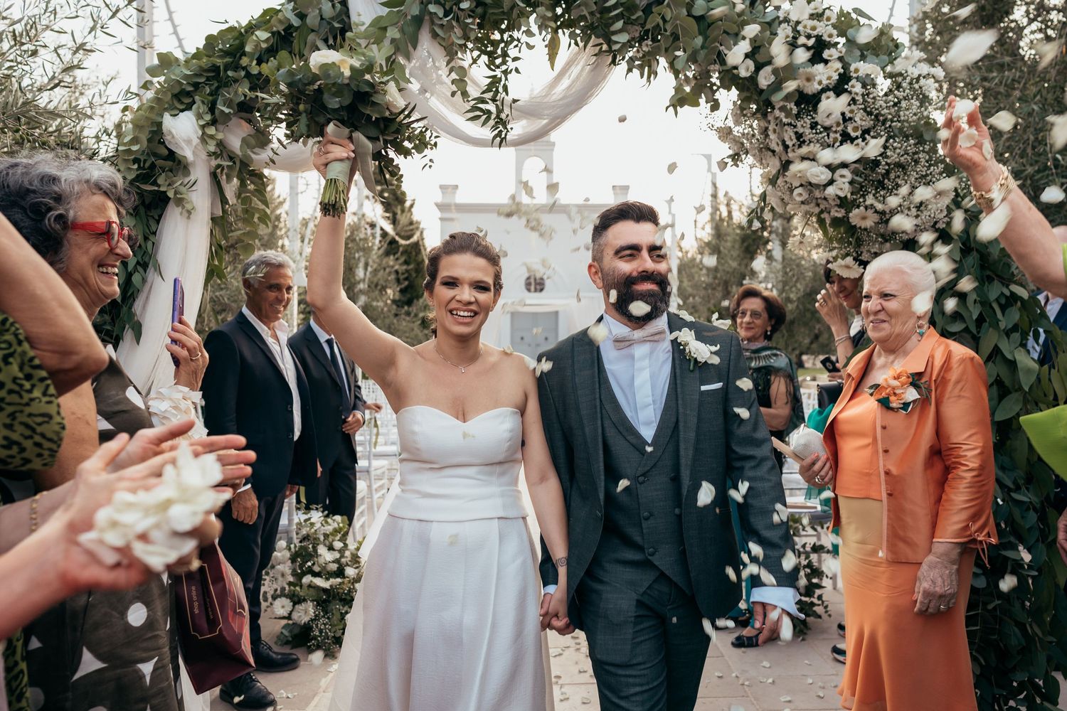 Wedding celebration under floral arch with guests throwing confetti during recessional.