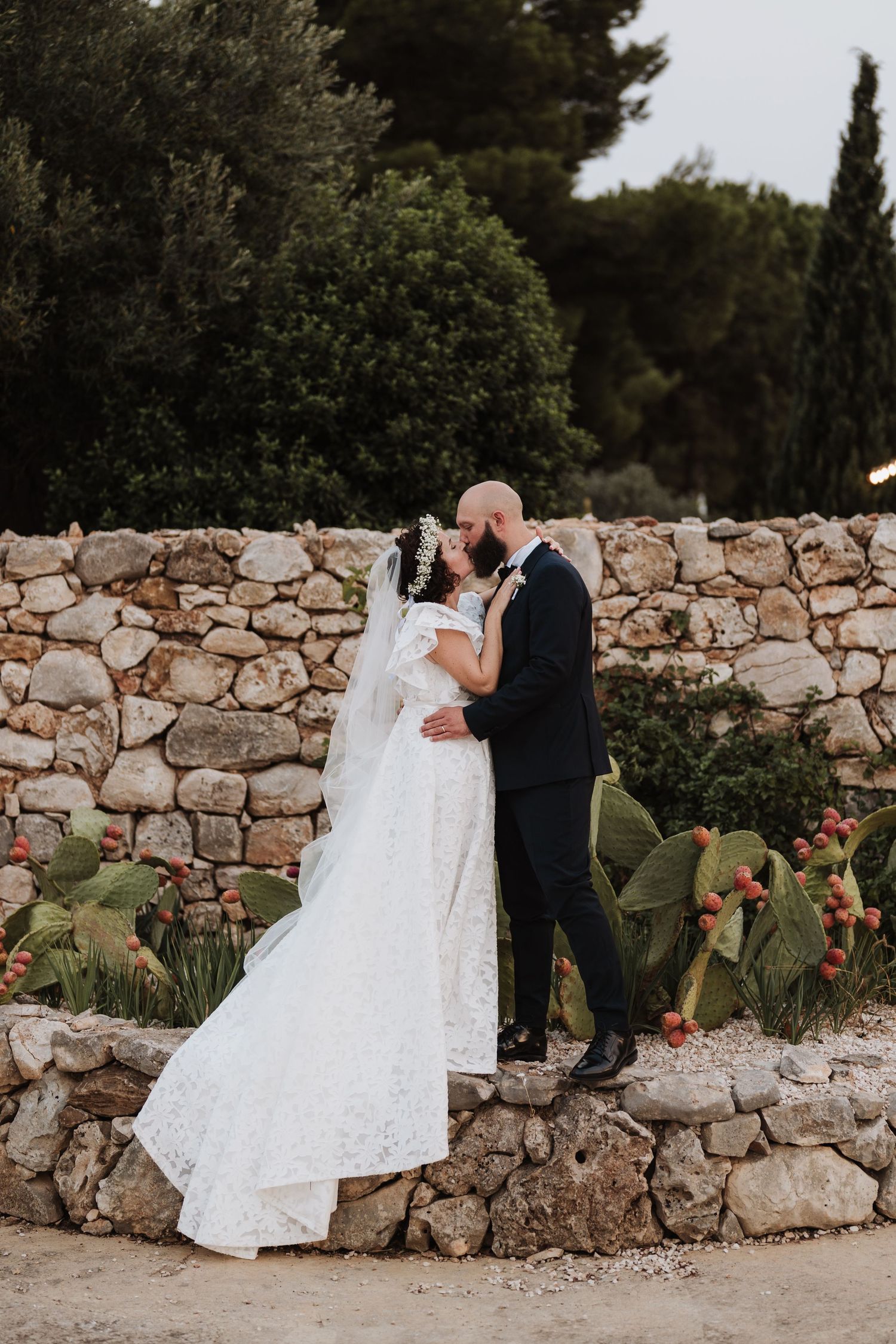 Romantic moment between newlyweds against rustic stone wall with cacti garden.