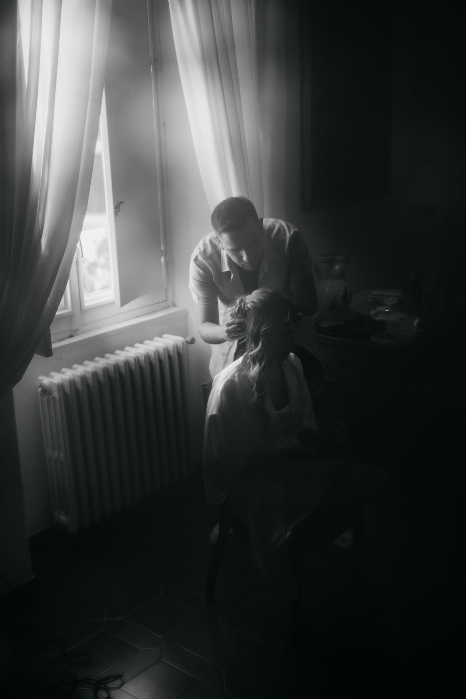 A moody black and white photo series showing a figure seated by a window with dramatic lighting and curtains.