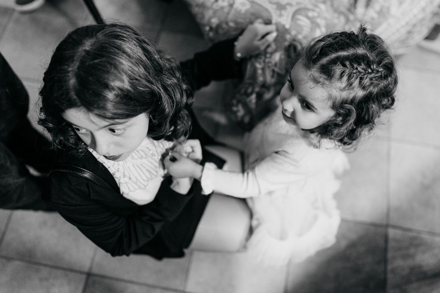 Two young girls holding hands and interacting in a black and white candid photo taken from above.