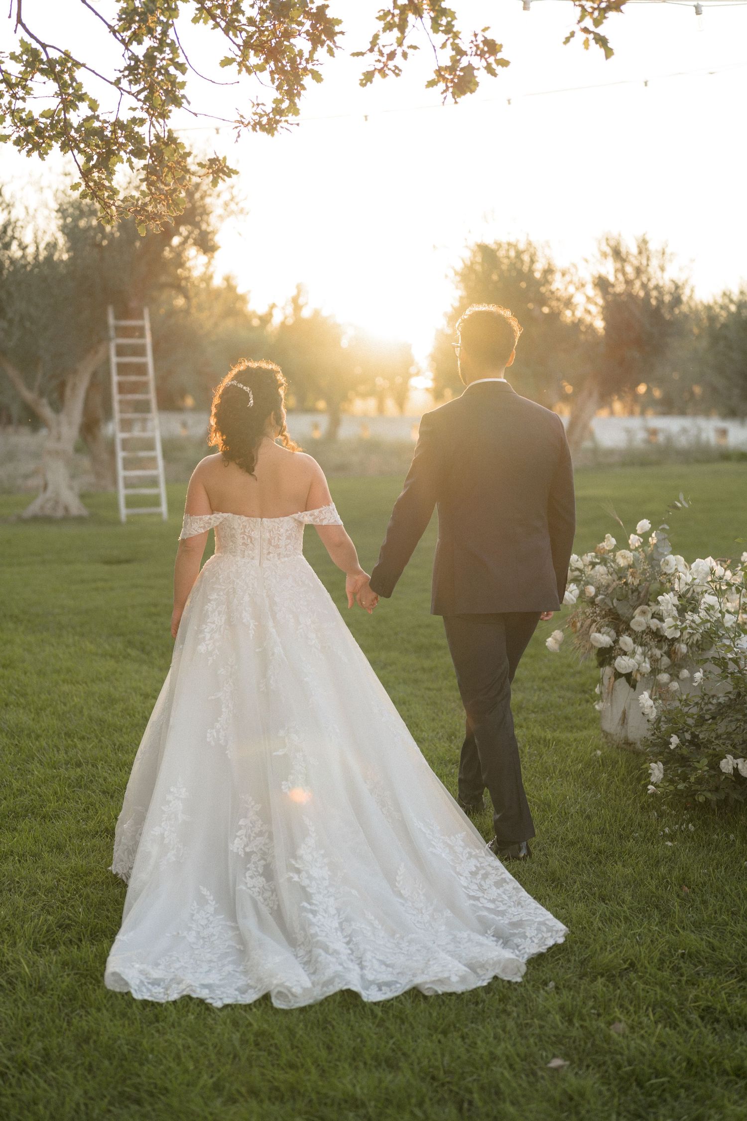 Bride and groom walking hand in hand through a sunlit garden at golden hour after their ceremony.