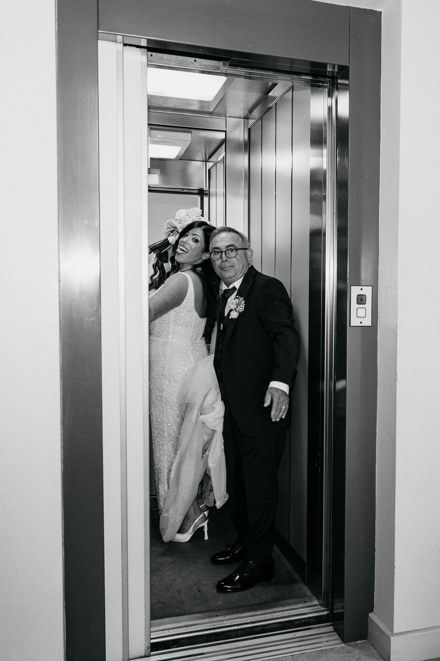 Bride and groom sharing a joyful moment in an elevator, captured in elegant black and white wedding photography.
