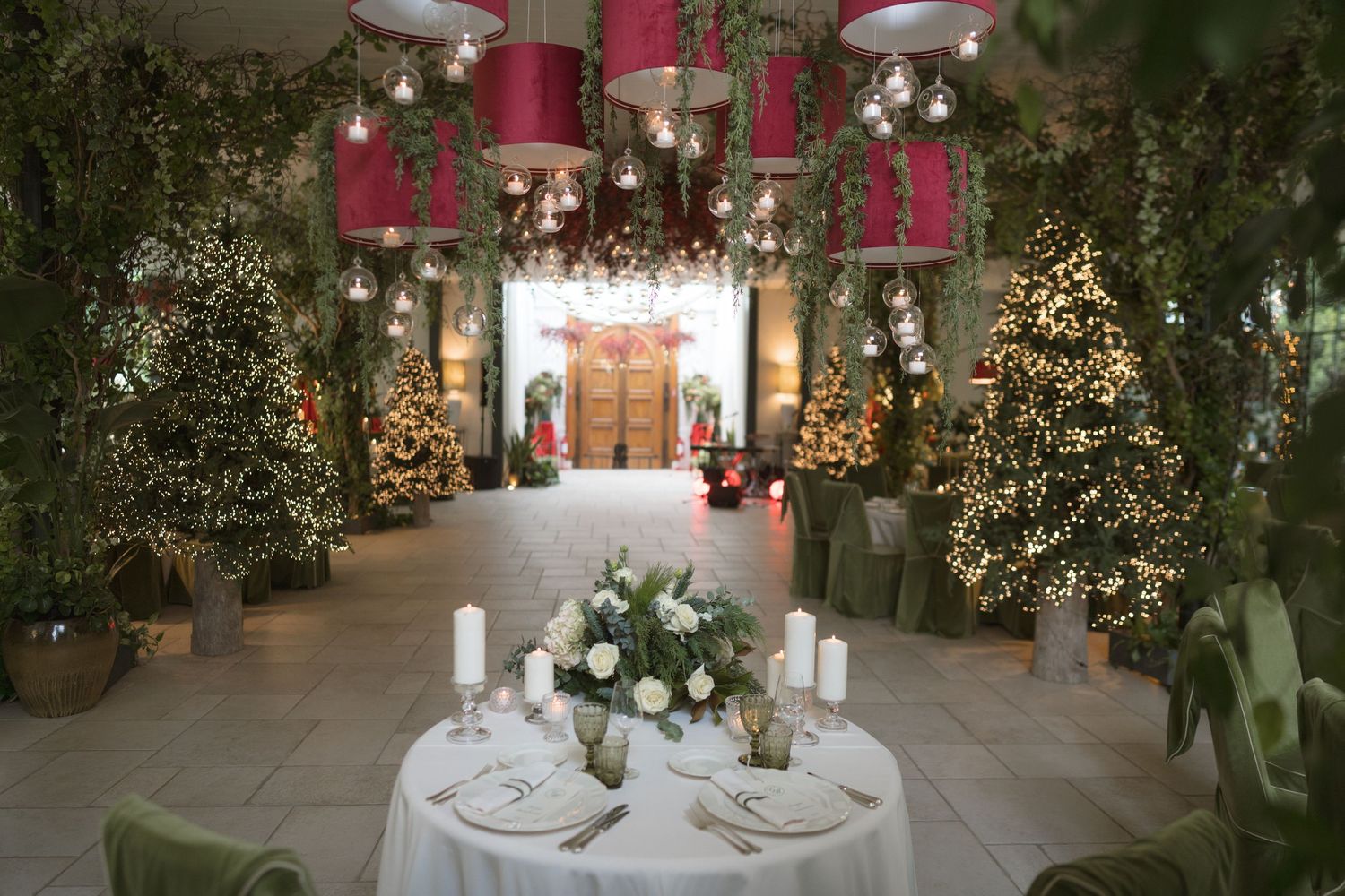 Festive wedding venue with Christmas trees, pink pendant lights, and white centerpiece.