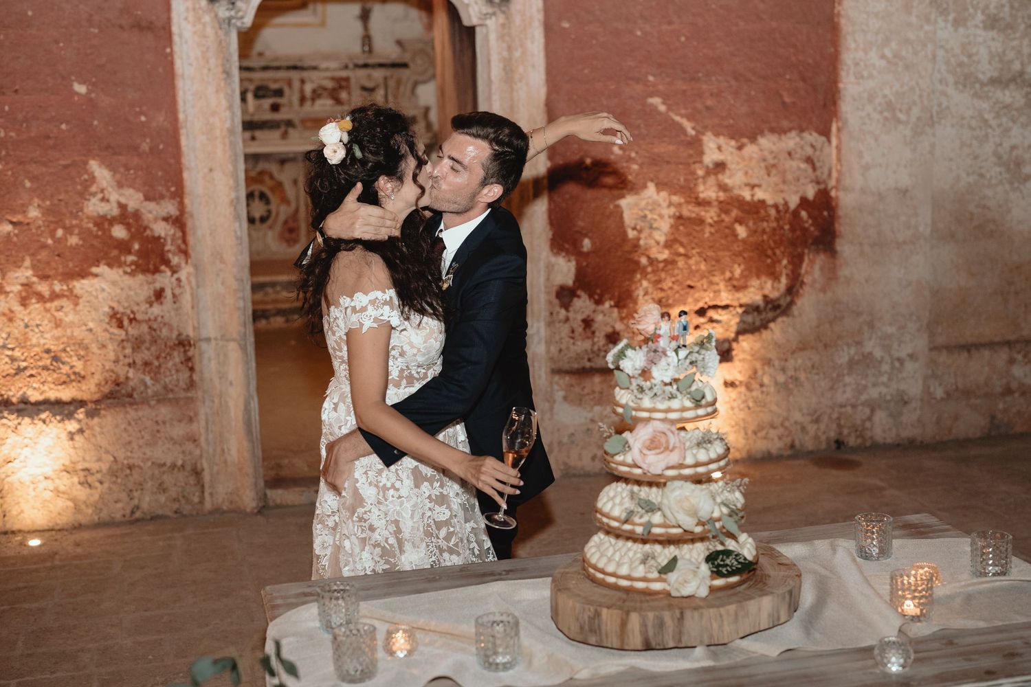 Wedding couple sharing a joyful moment next to their elegant tiered cake in a rustic venue.
