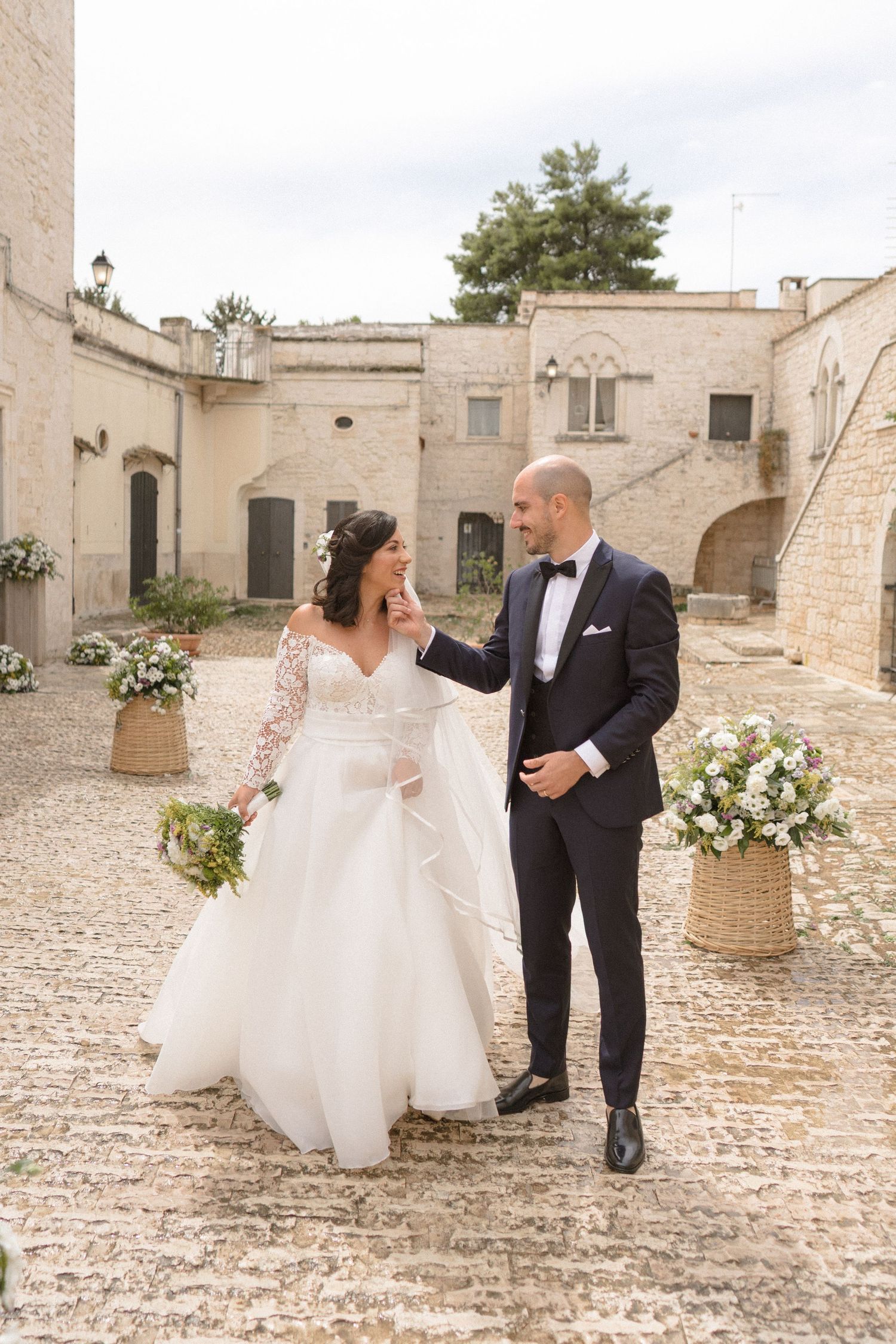 Wedding couple posing for photos on cobblestone courtyard with stone architecture.