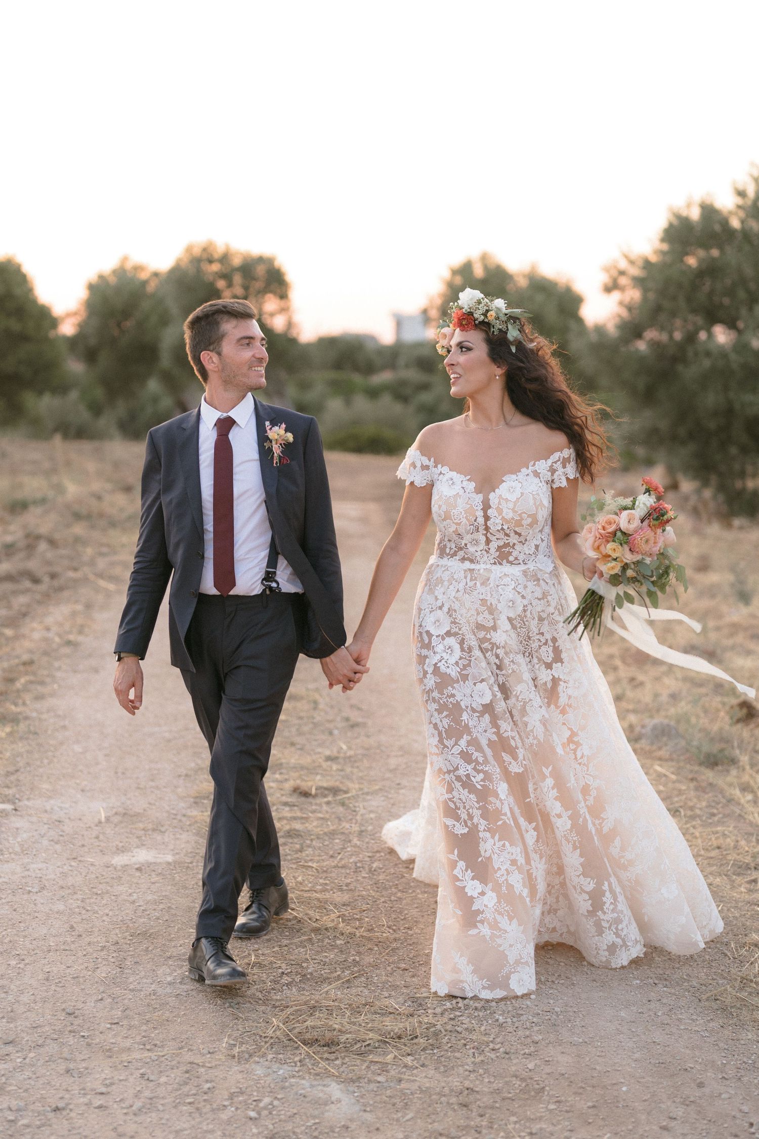 Couple walking and laughing together on a desert path during sunset in wedding attire.
