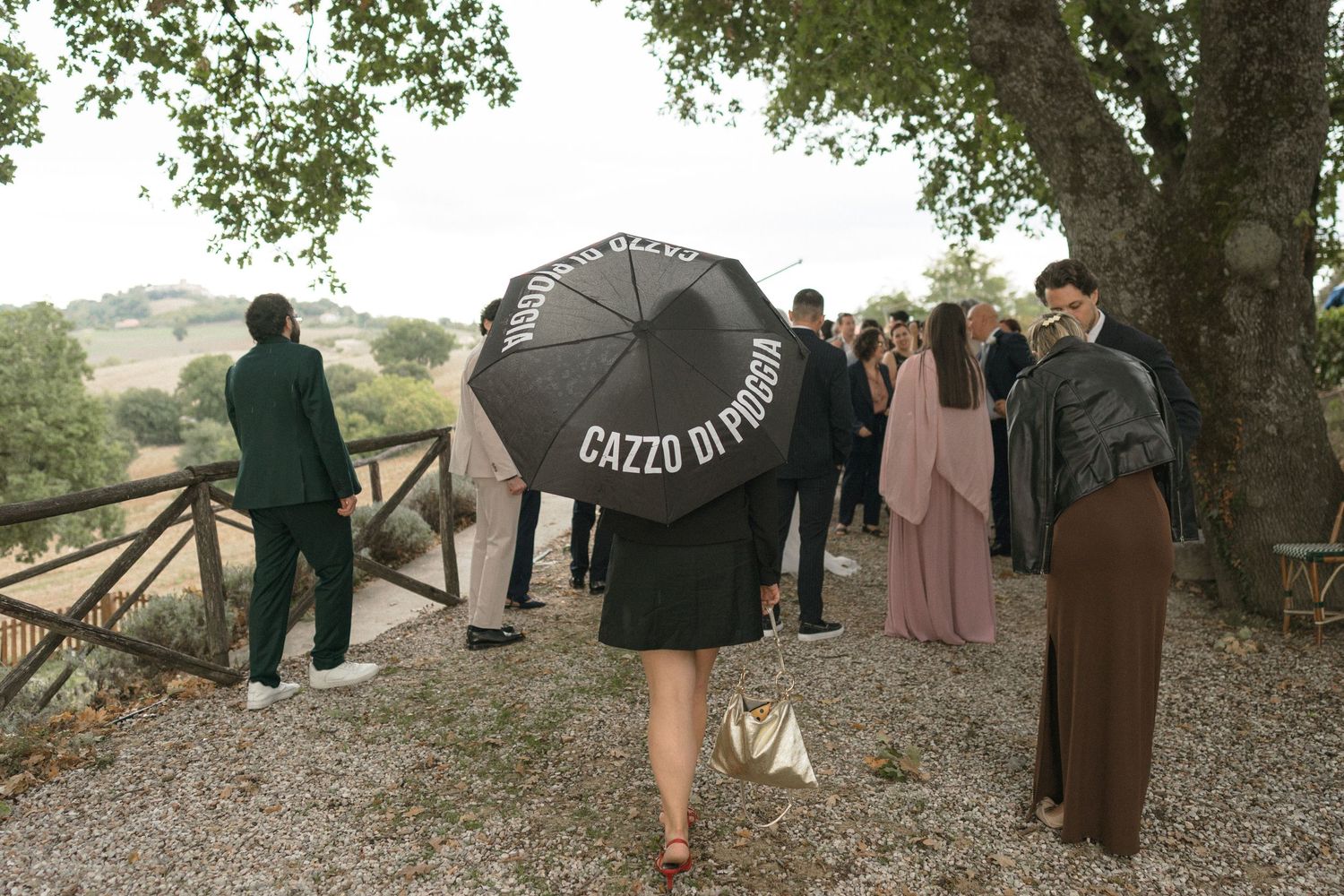 Wedding party gathered under trees with umbrellas during an outdoor celebration.