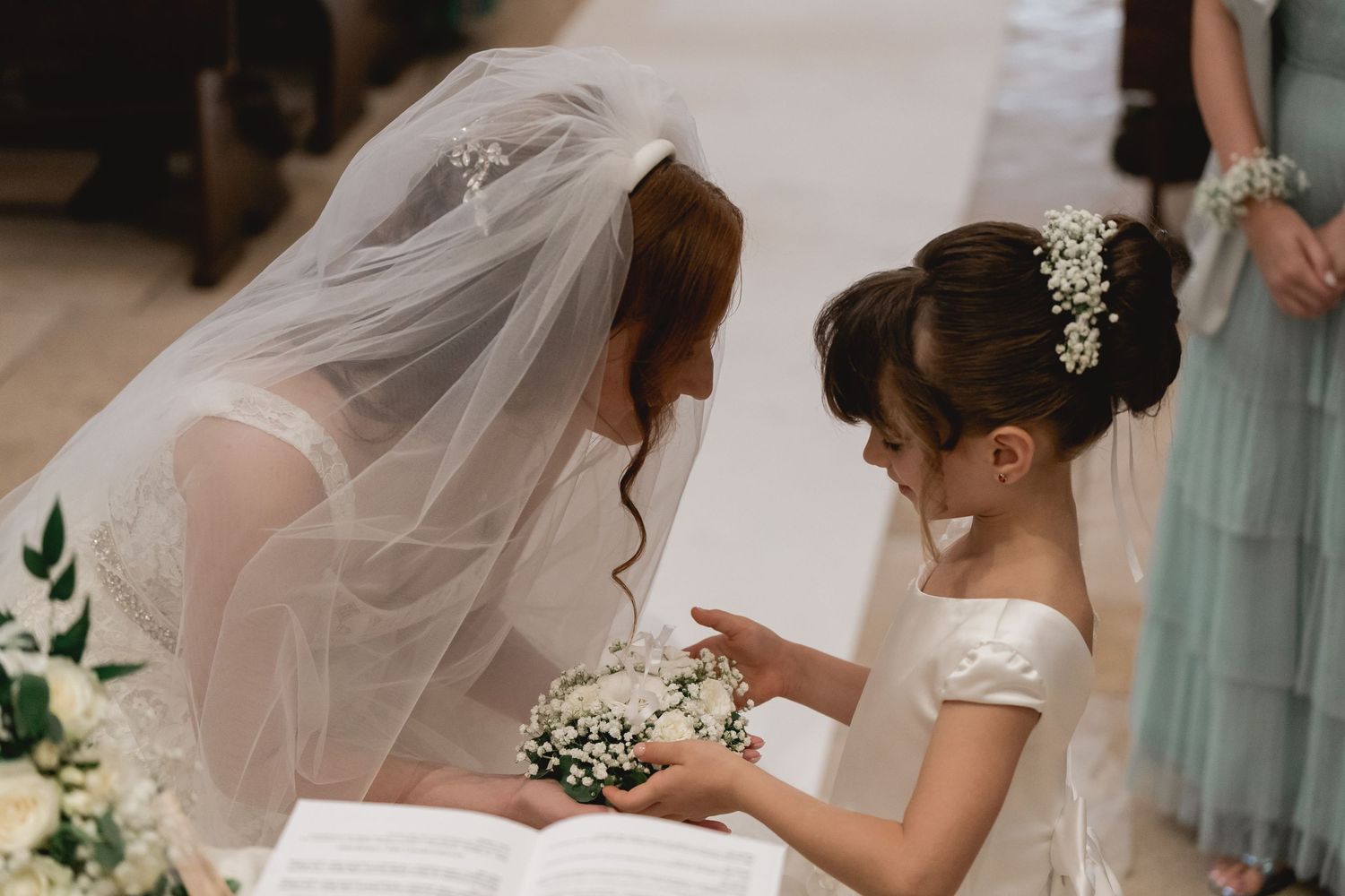 Sweet moment between bride and young attendant sharing flowers during wedding ceremony.