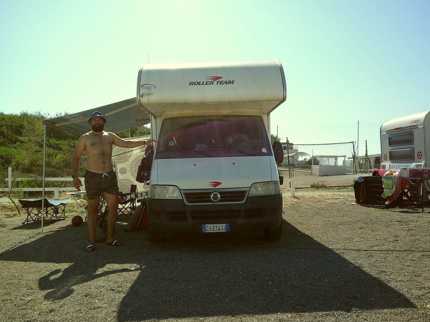 A white RV camper van parked in a sunny parking lot with desert landscape in the background.