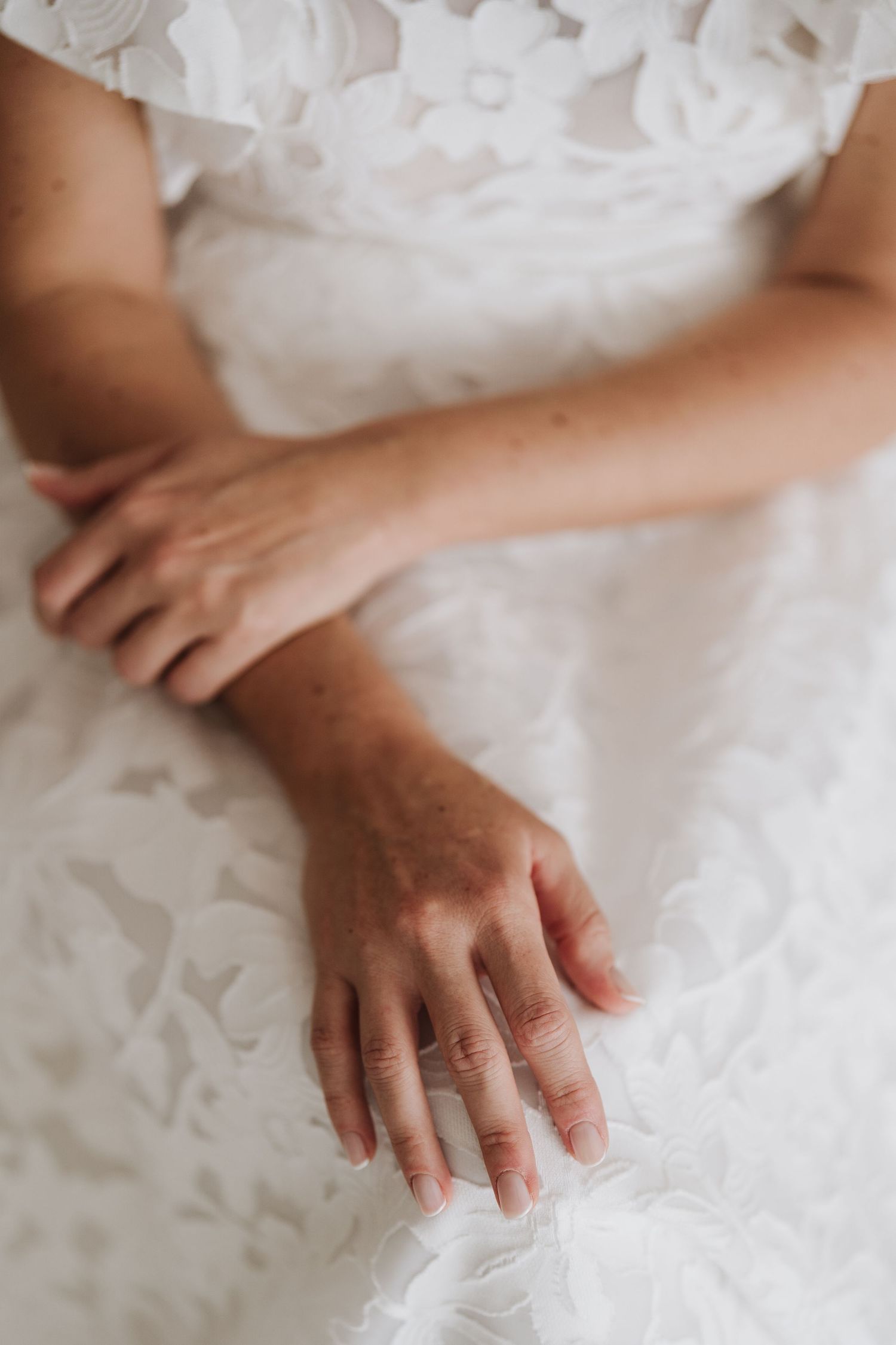 Hands resting on white lace fabric with delicate details.